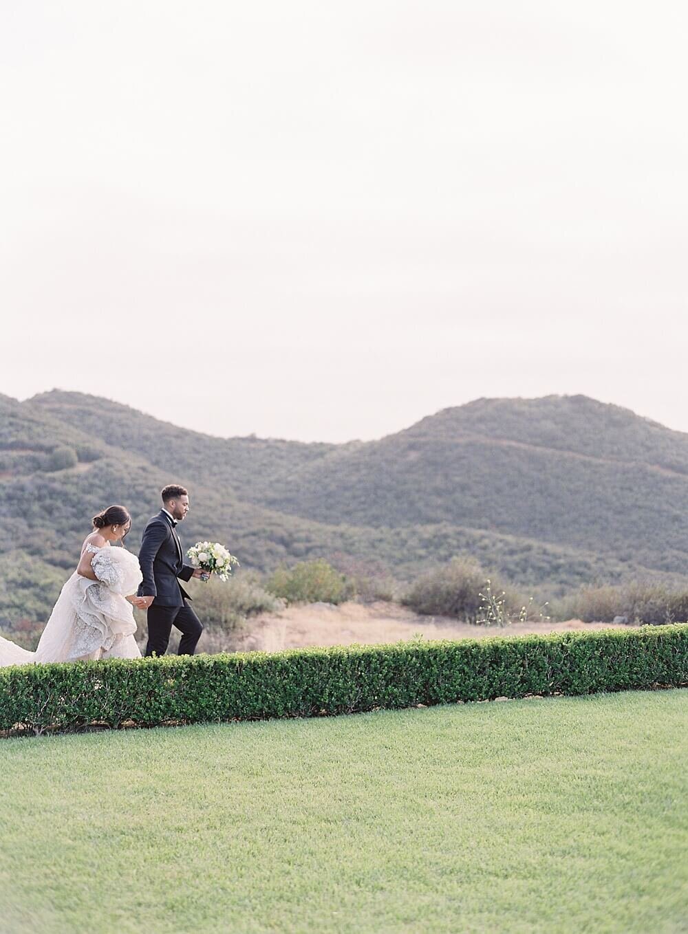 bride and groom walk across grass with mountains at cal-a-vie  | Jacqueline Benét