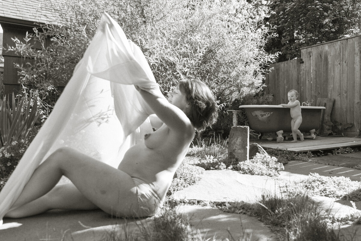 Black and white image of mother and toddler daughter in the backyard with bathtub