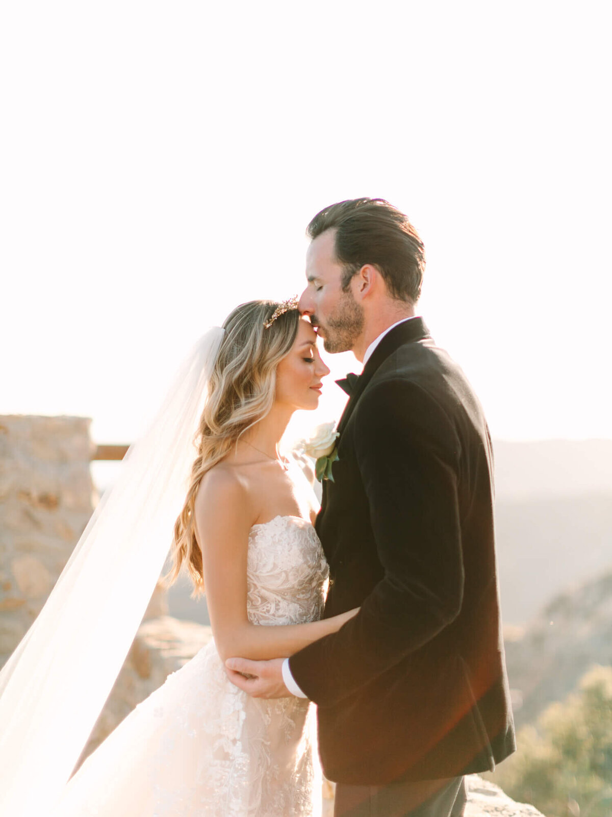 A bride and groom share an intimate moment, the groom kissing her forehead.
