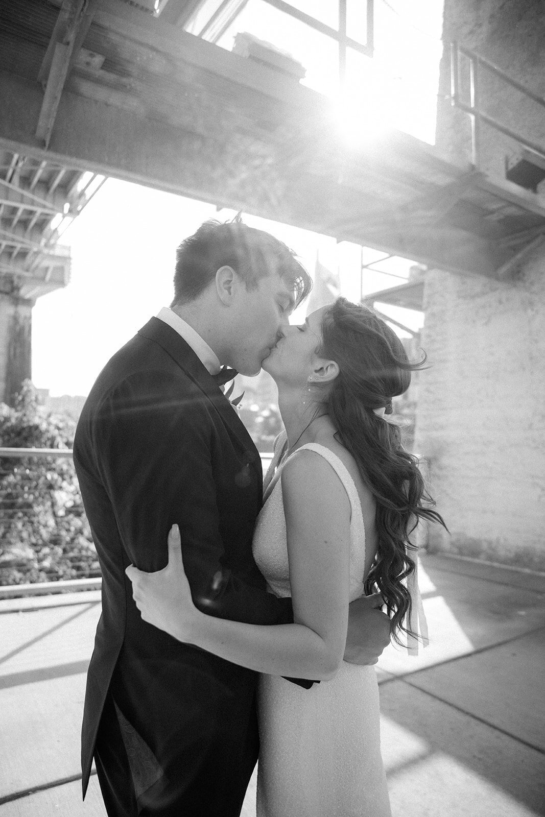 Newlyweds embrace with a kiss in a black and white photo shot under the Pedestrian Bridge in downtown Nashville, TN.