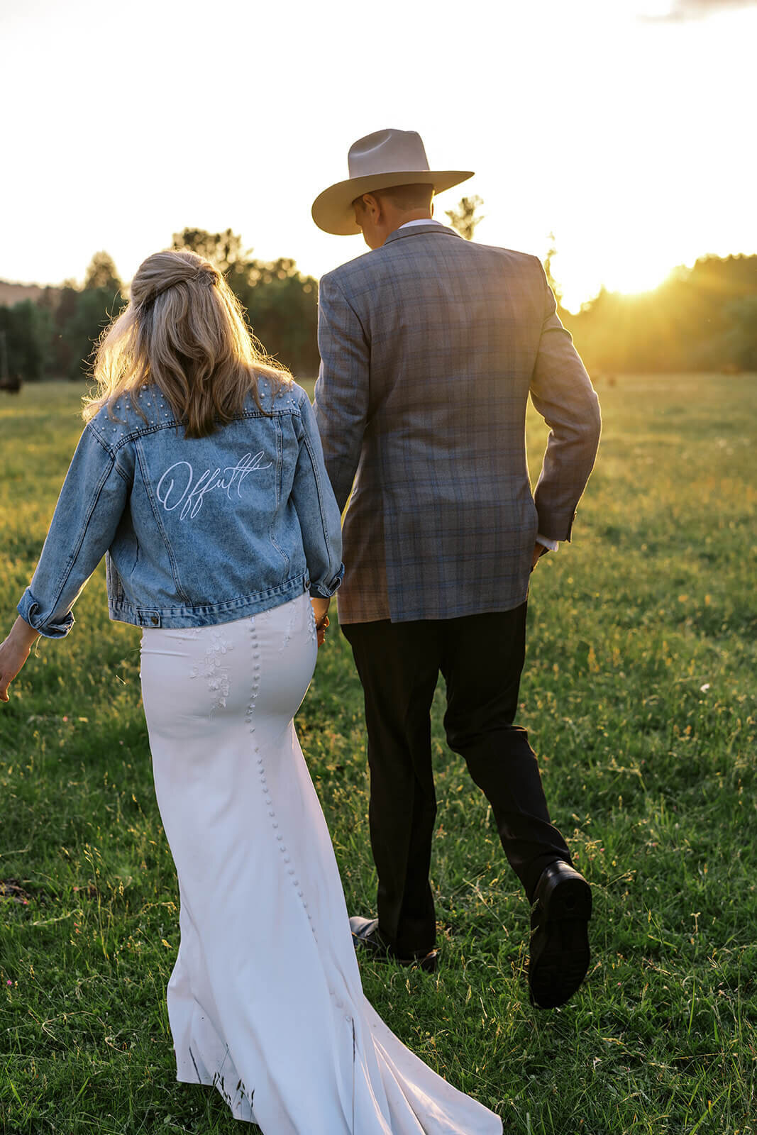 A bride and groom walk in a field facing away from the camera.