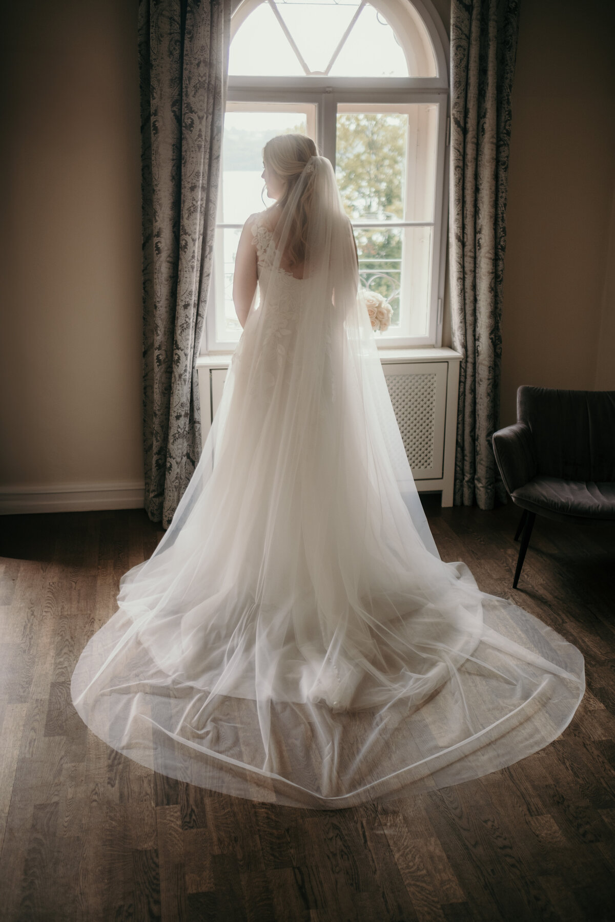 The bride stands in front of a window showing the back of her georgeos dress.