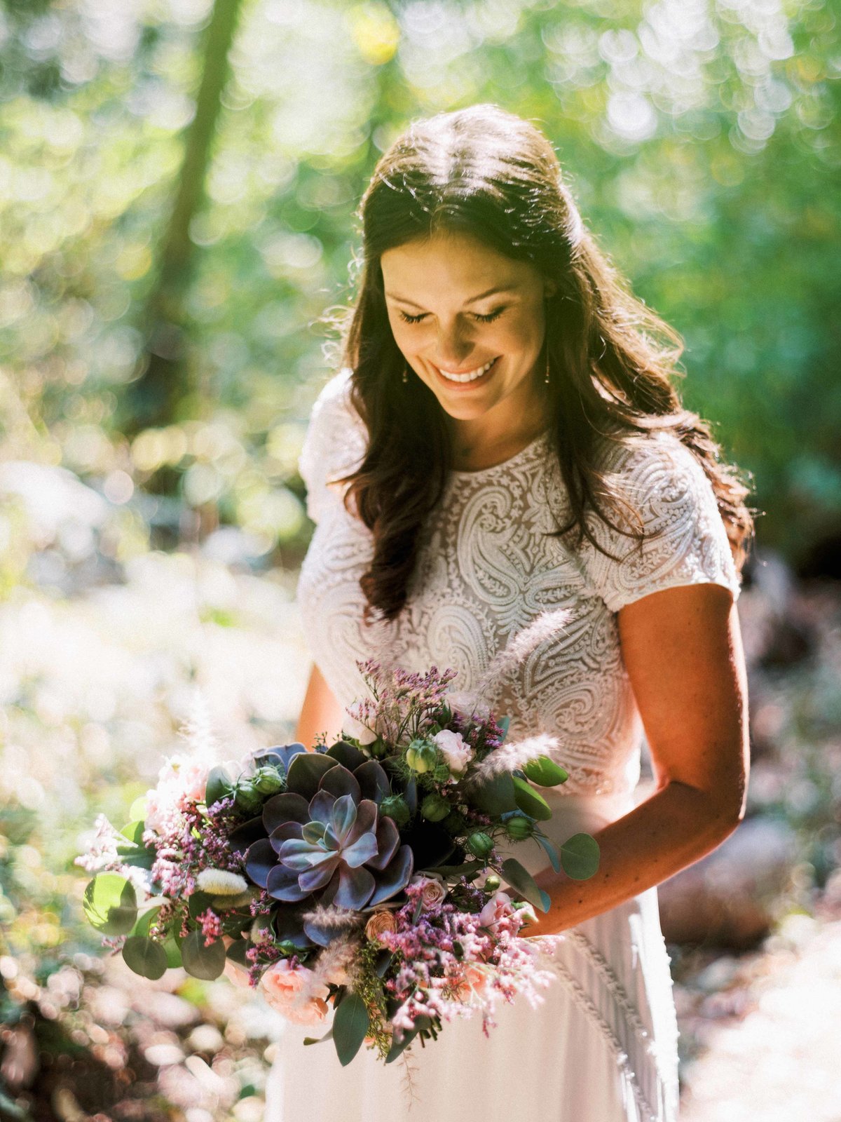 Our beautiful bride in the sun holding a bouquet of succulents, grasses, pods and spray roses.