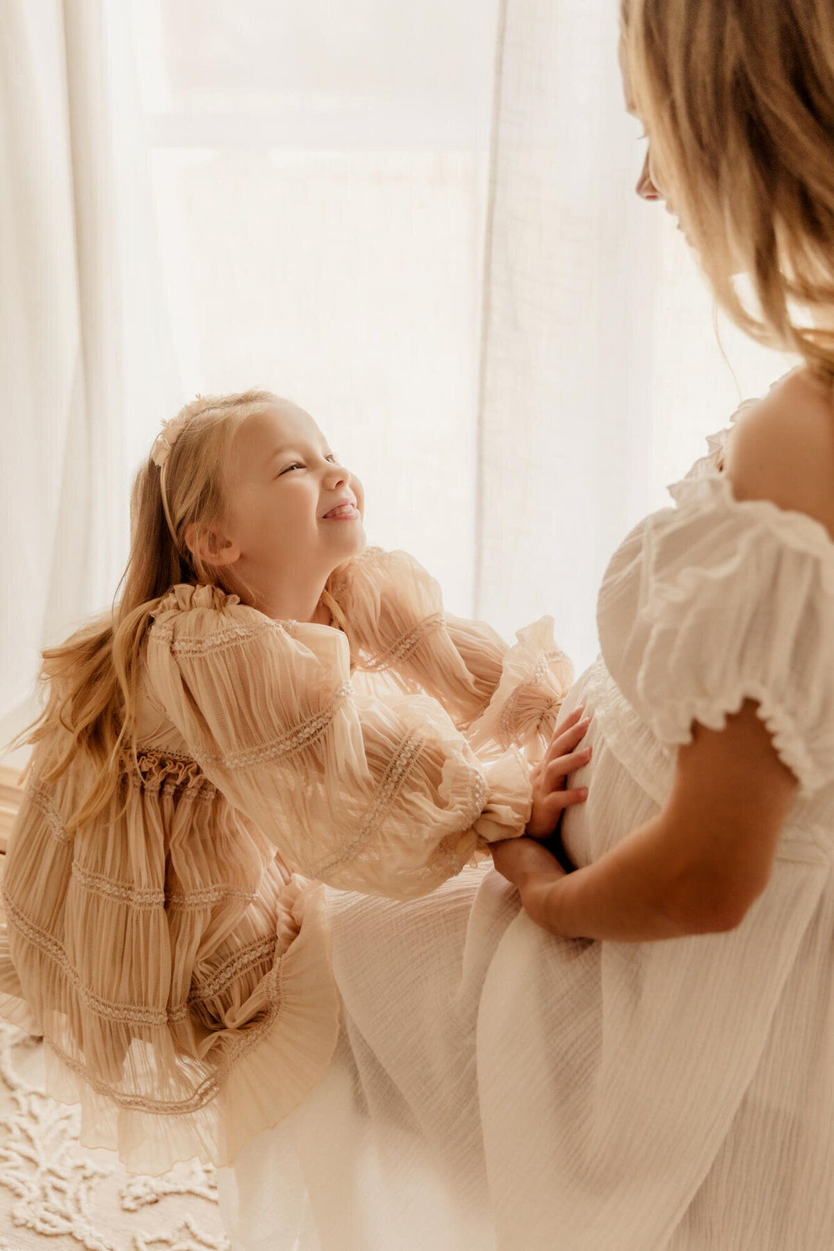 Girl smiles at her expecting mother while holding her mom's pregnant belly for a maternity photo session in OKC.