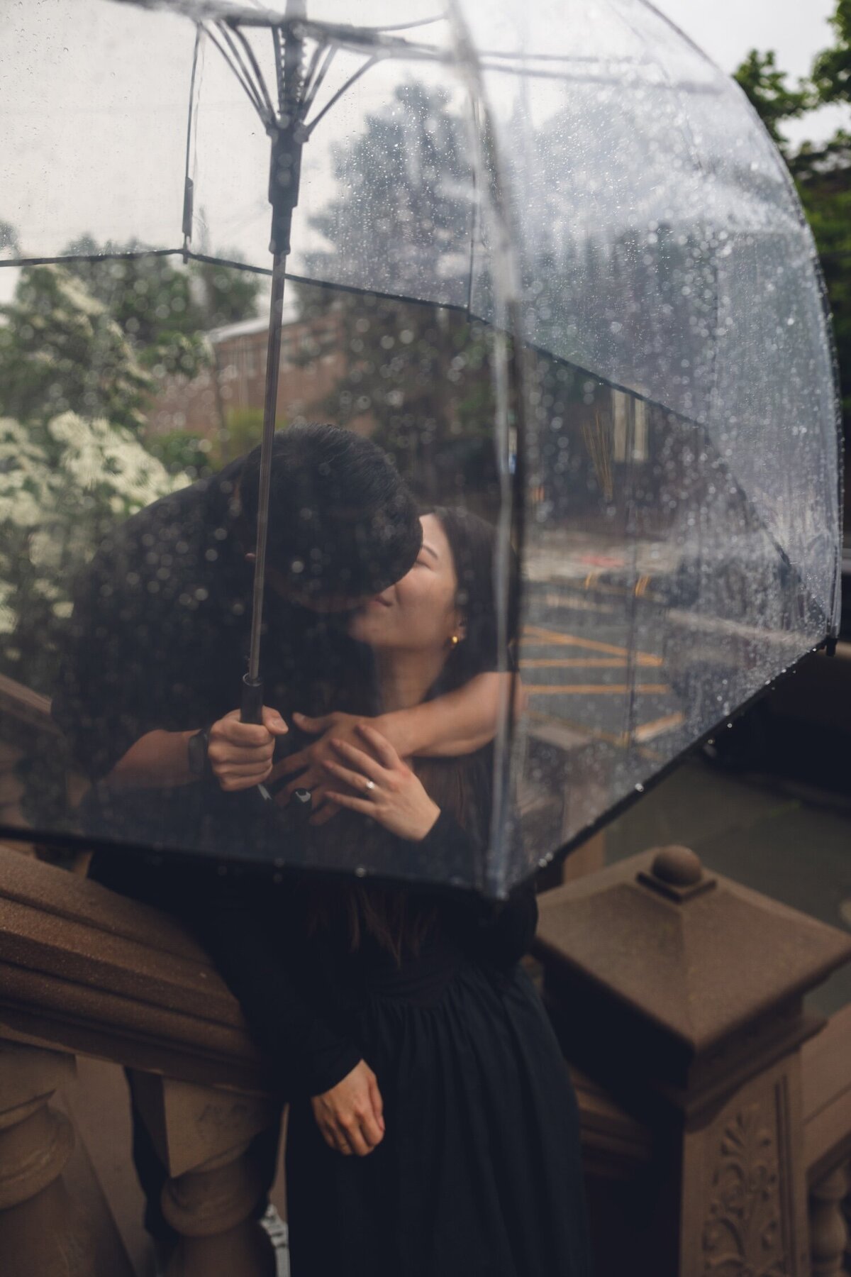 Couple kissing on rainy brownstone steps with umbrella

