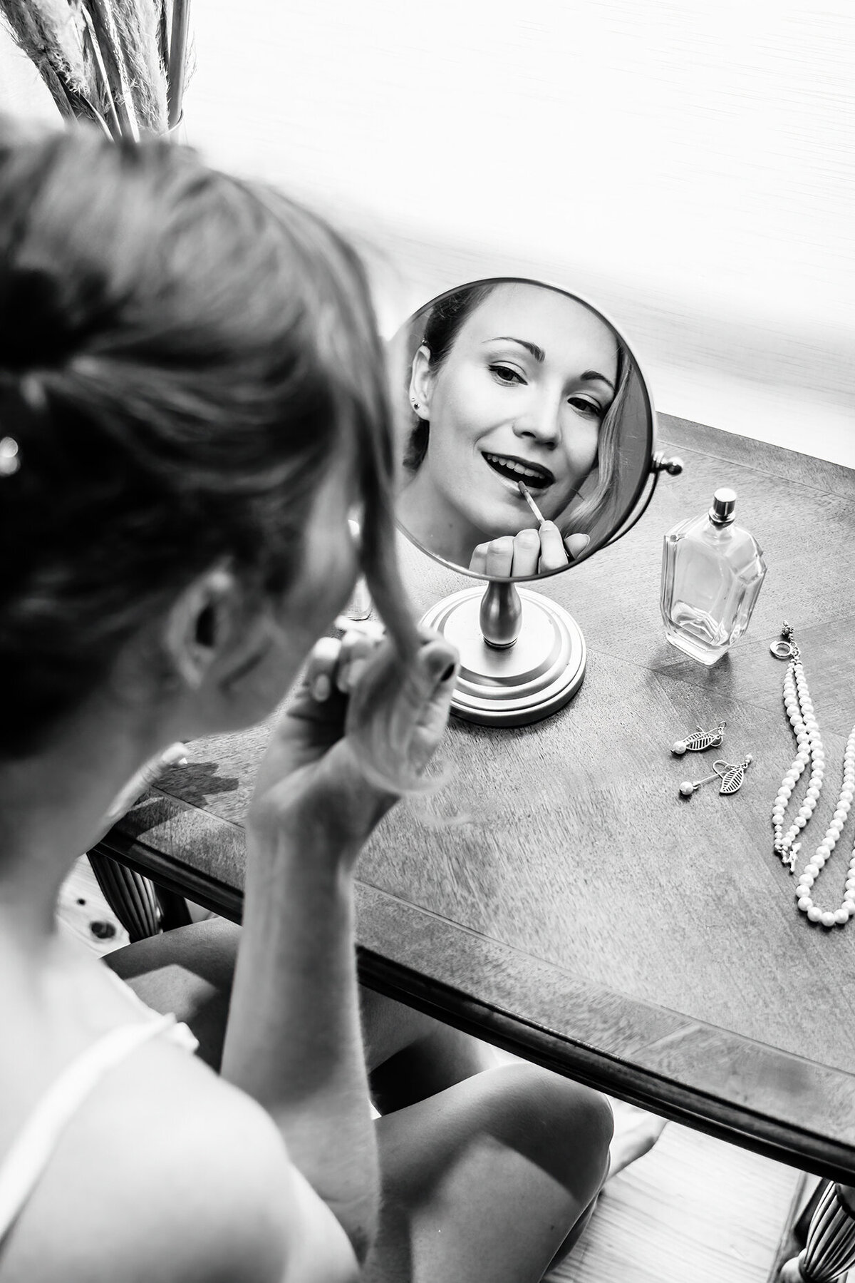 a artsy photo of a bride putting lipstick on while looking in a mirror.