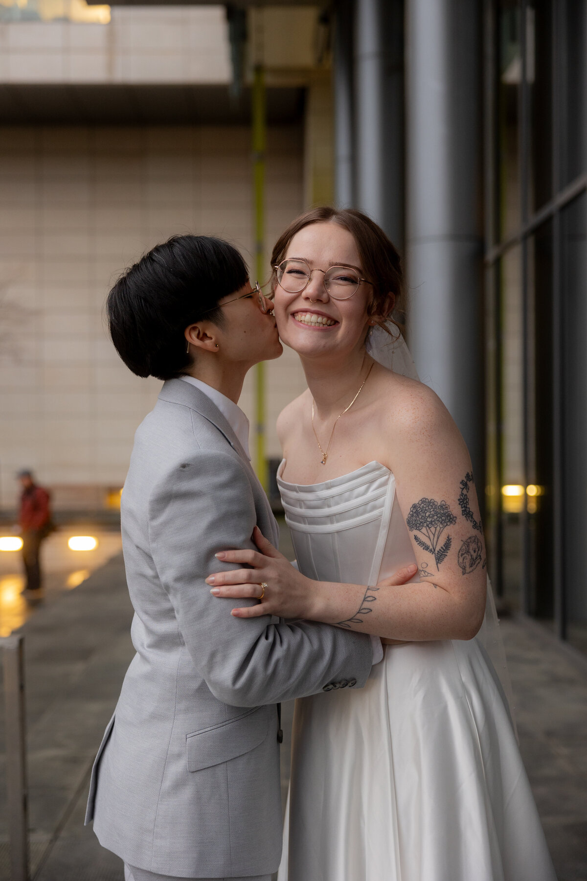 A sweet and intimate moment as the bride gently kisses her fiancé on the cheek outside the Seattle Courthouse, capturing the joy and affection of their wedding day.
