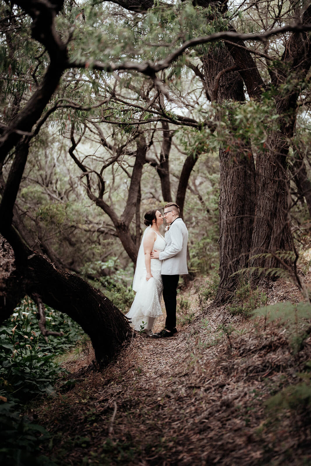 Wedding portrait of two brides kissing under trees