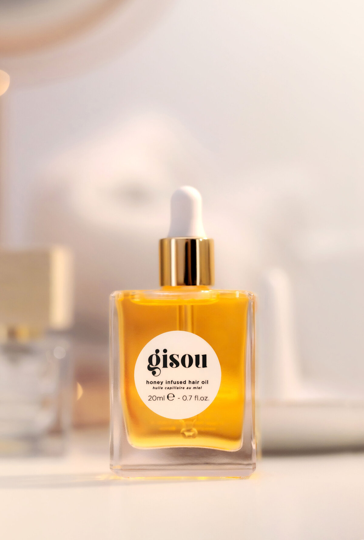 Photo lifestyle de l’huile capillaire Gisou sur fond blanc lumineux, réalisée par Studio Helloday.