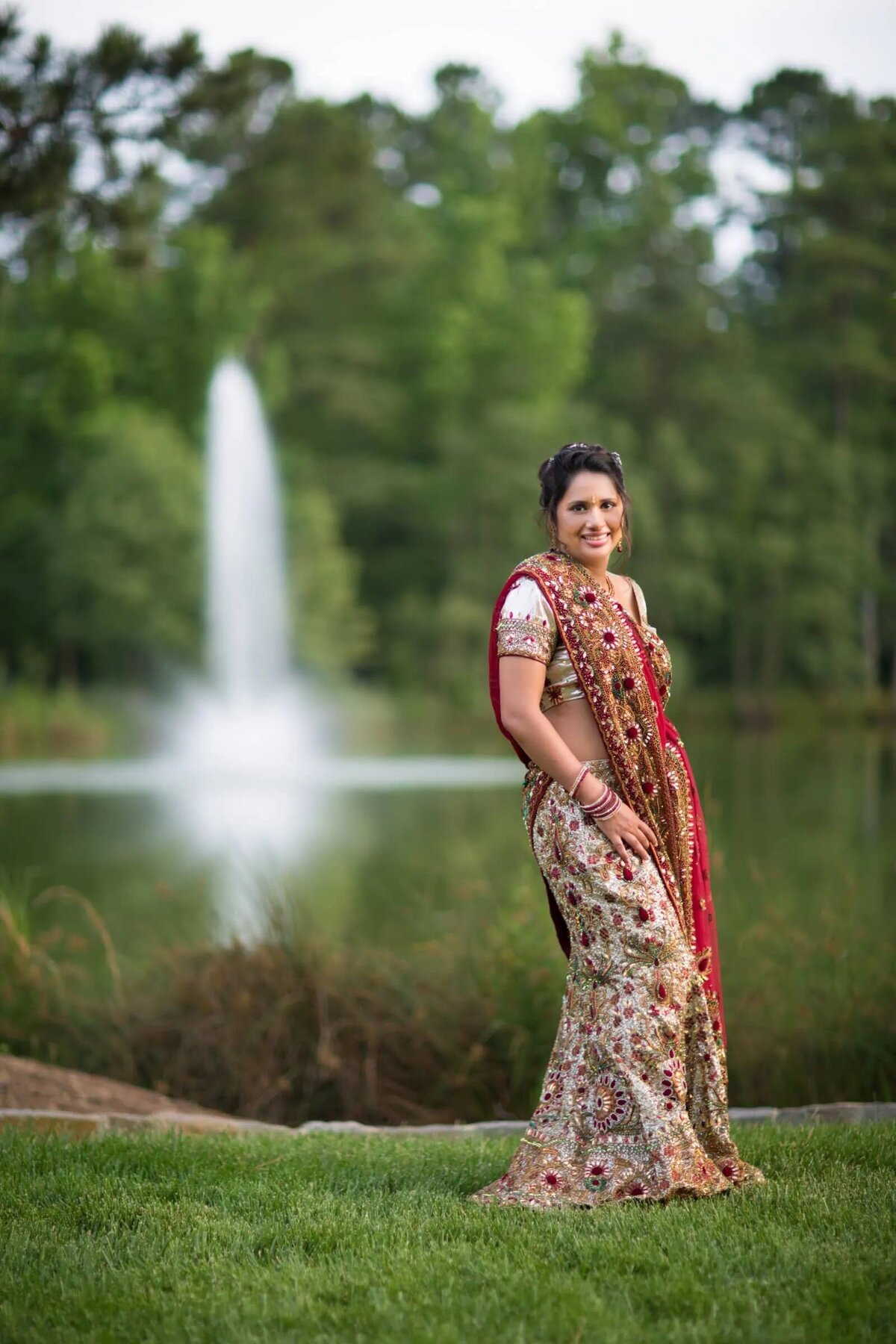 A bride in traditional Indian clothes standing in front of a lake