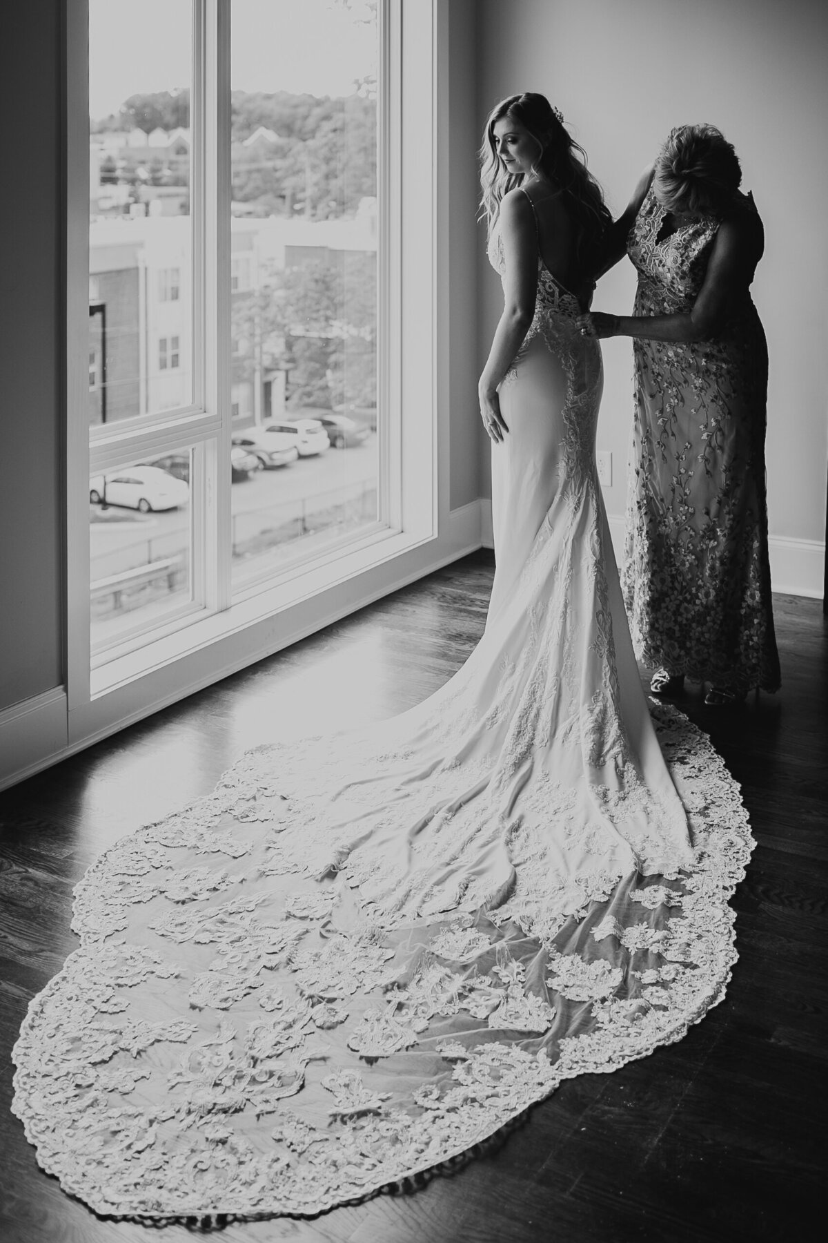 bride with her mom before wedding putting on her dress
