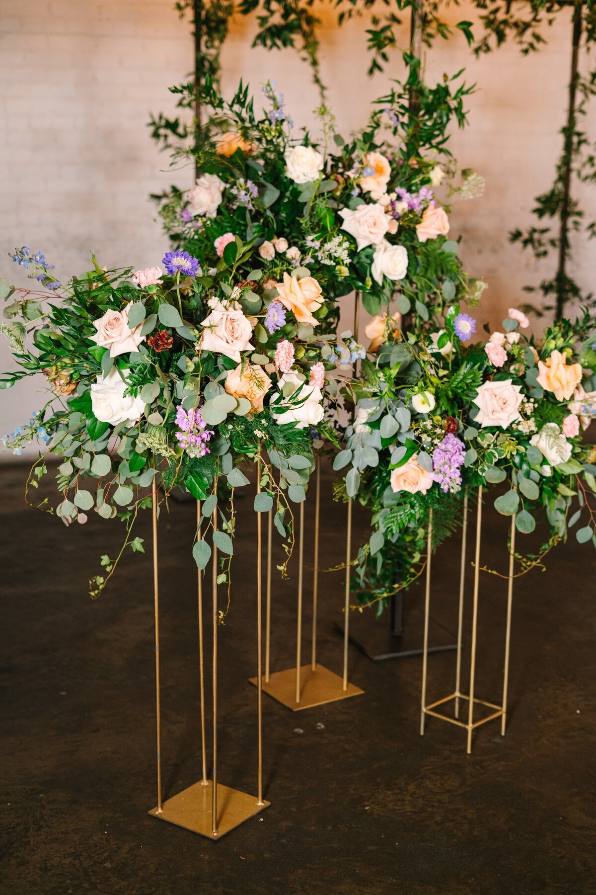 Light colorful floral arrangements on gold stands filled with orange, purple, and peach flowers.