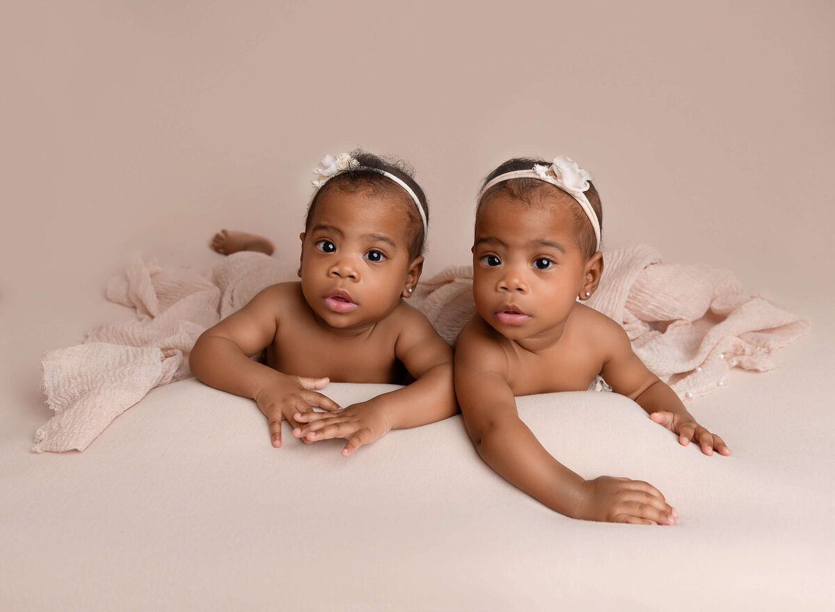 Twin 6-month-old girls propping their heads up and smiling at the camera for their milestone photoshoot in  NYC