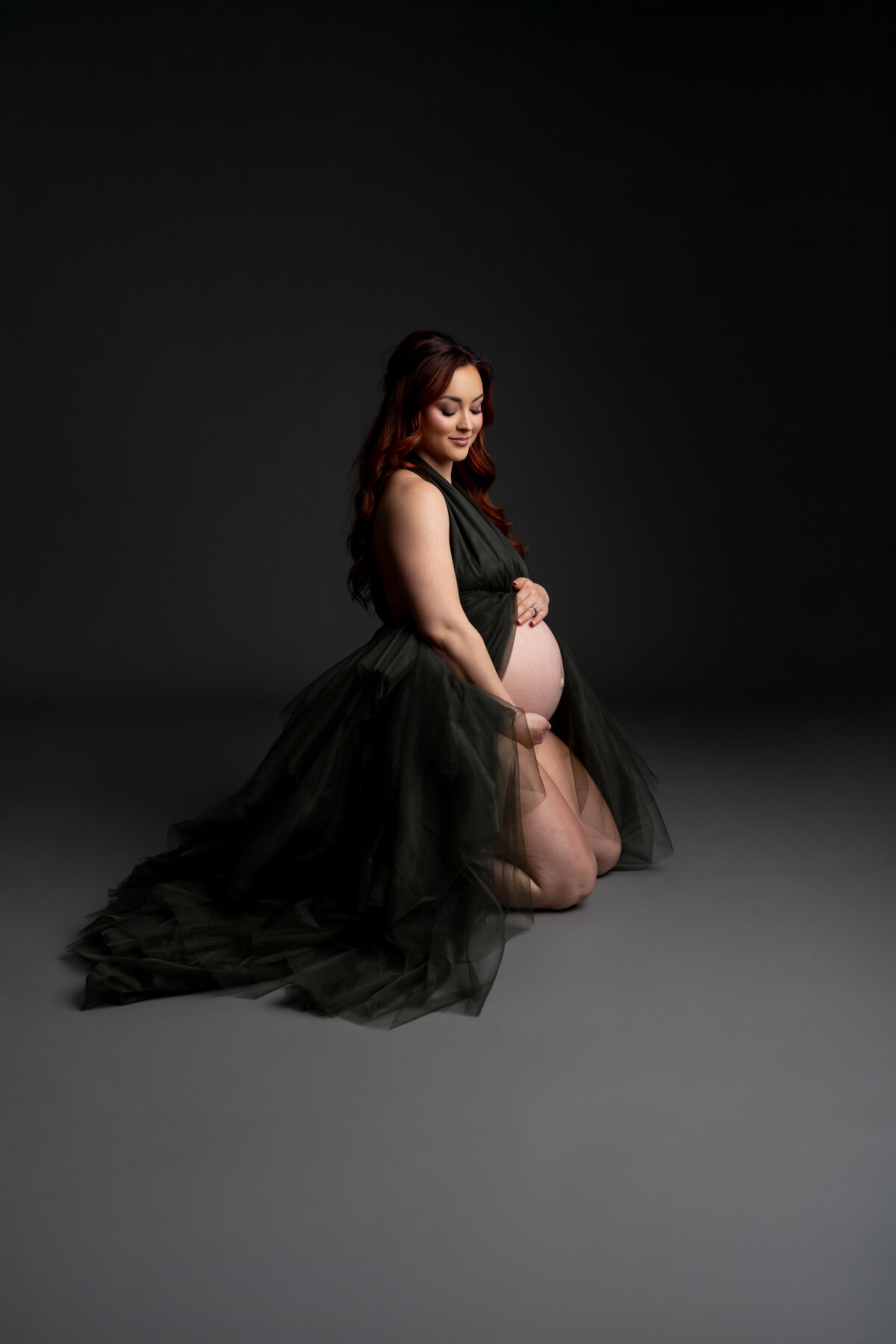 Kneeling in a black dress, she is softly illuminated, her serene posture exuding elegance and calm. Captured by Inland Empire photographer Kaitlyn Dawn Photography.
