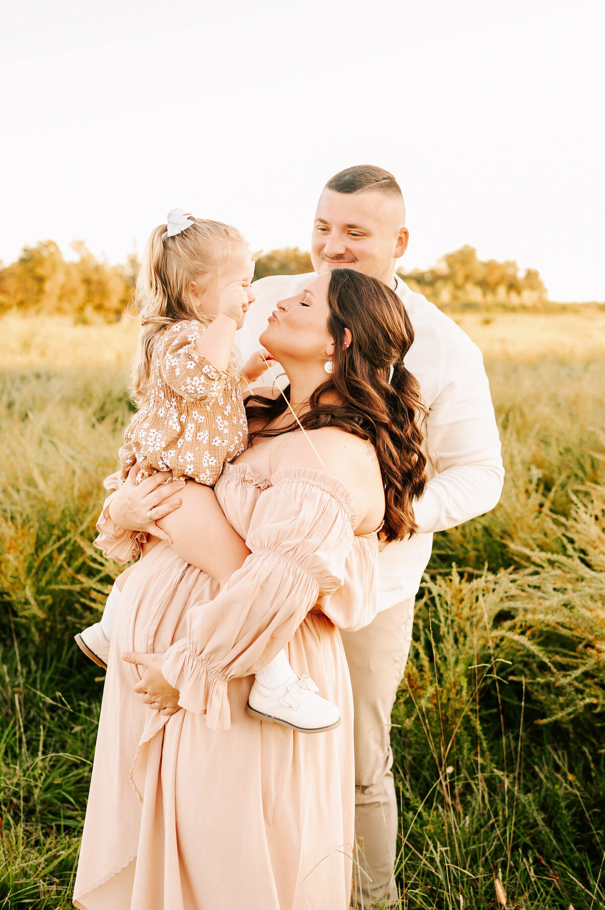 Pregnant mom kissing toddler in a field during Branson MO maternity photography session