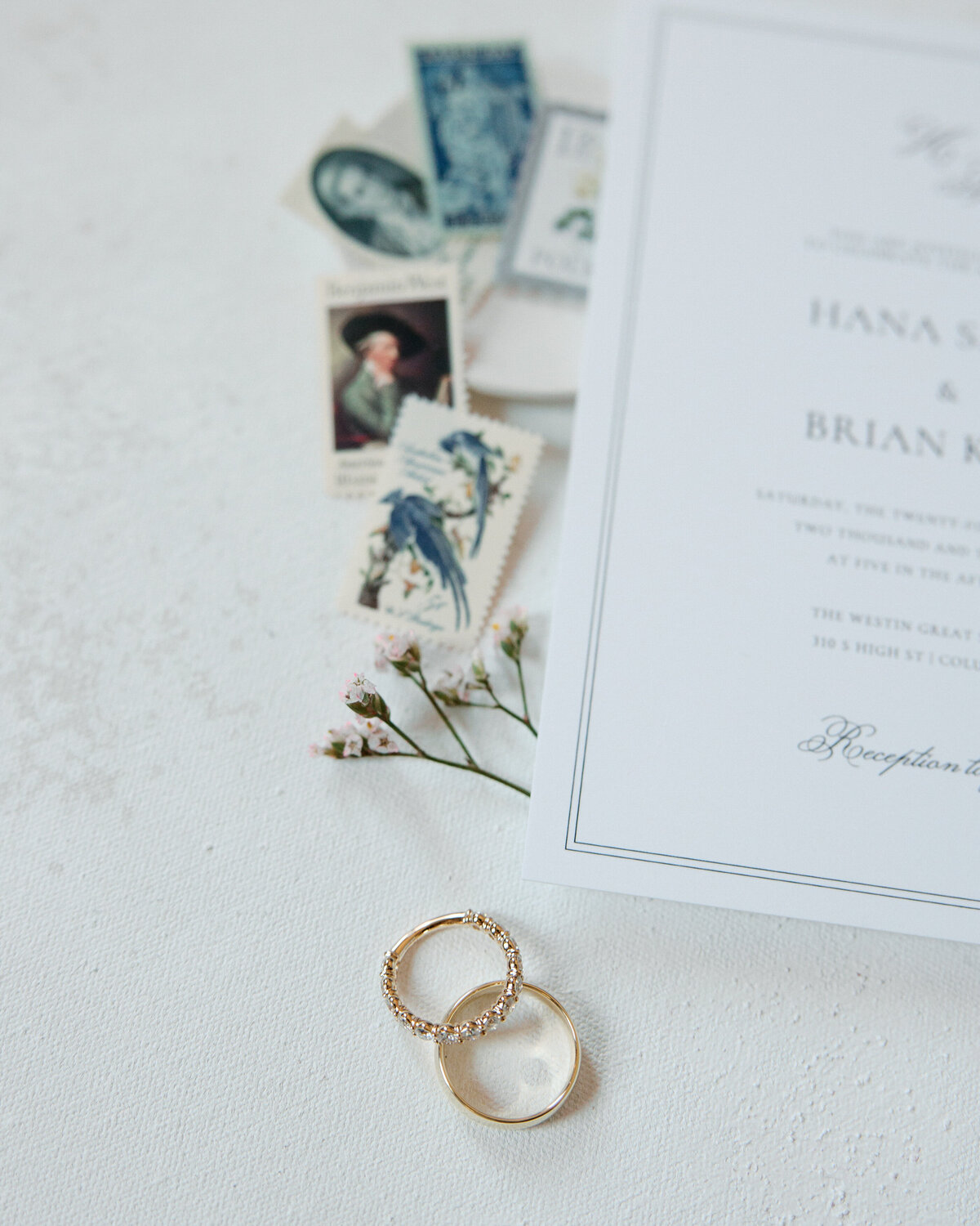 Close-up of gold wedding bands and vintage stamps on ivory paper, shot in natural light in Philadelphia.