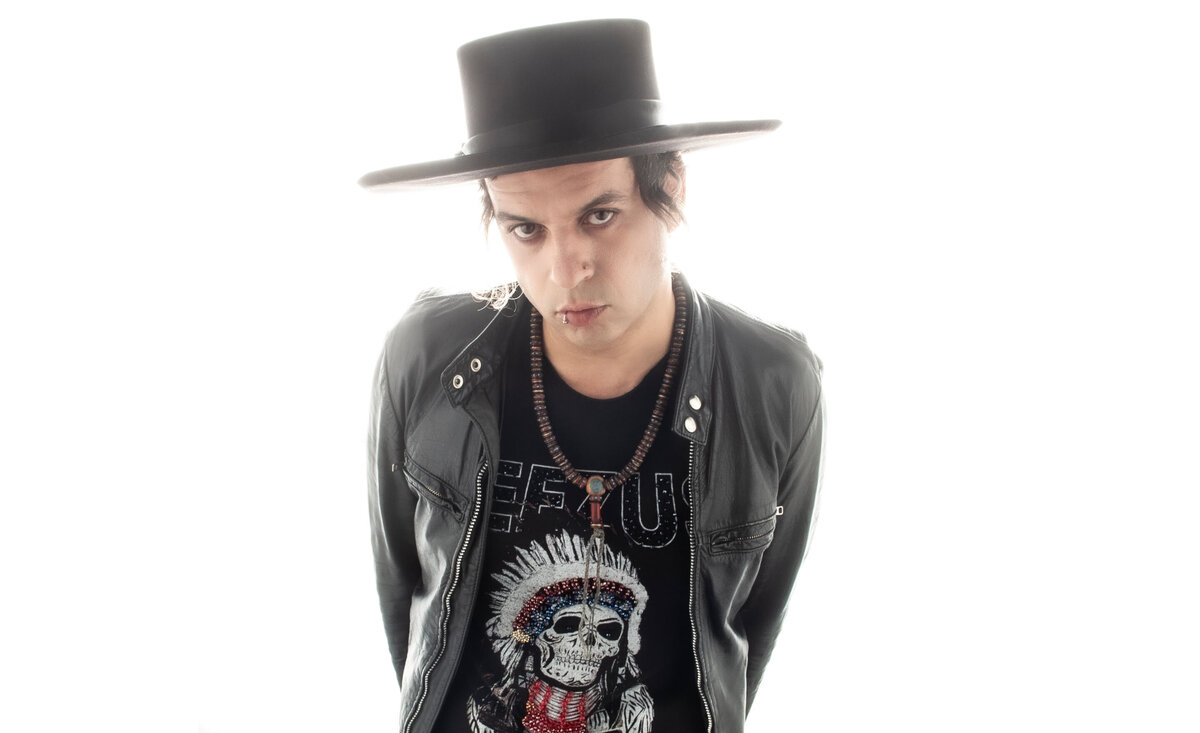 Male music artist portrait Fernando Basillio wearing black cowboy hat black leather jacket  against white wall