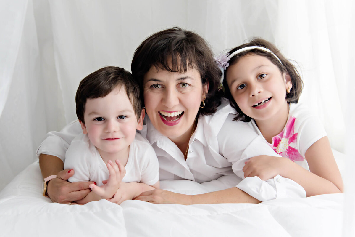 mom with her son and daughter laying on their belly's on a white bed for their family photography session in Burlington, ON