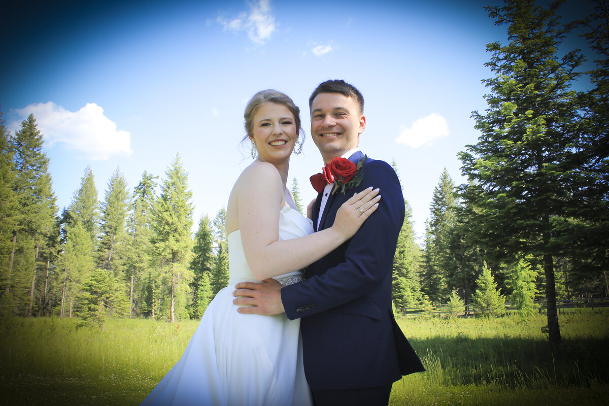 Bride and Groom in meadow on summer day smiling with pine trees in background