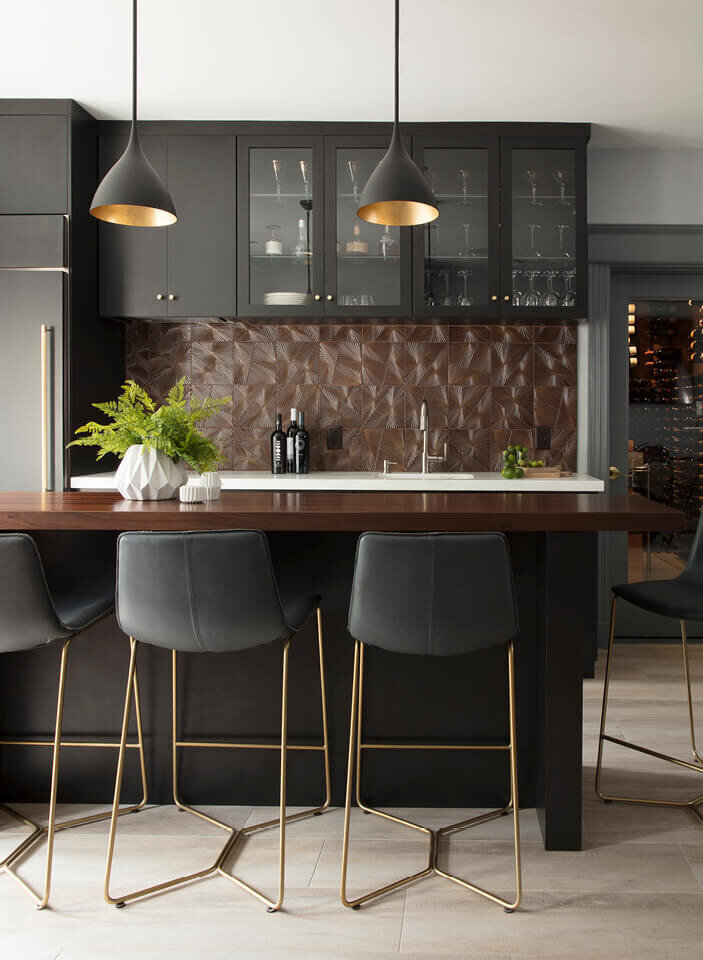 Interior Designers in Boston create a modern kitchen in a Westwood home with dark grey cabinets, an Ann Sacks backsplash, and Kelly Wearstler lighting.