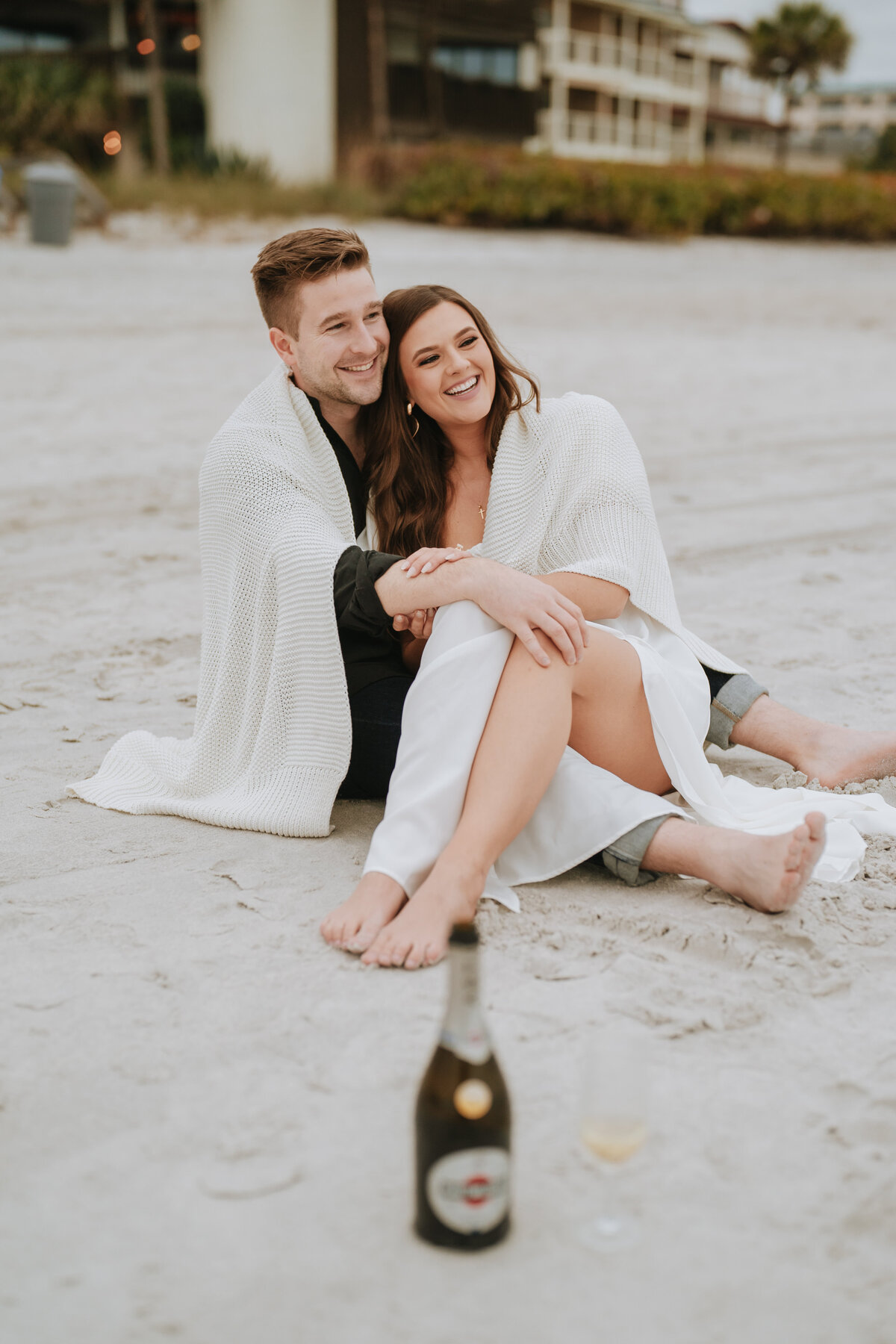 couple snuggled up on treasure island beach smiling during engagement session