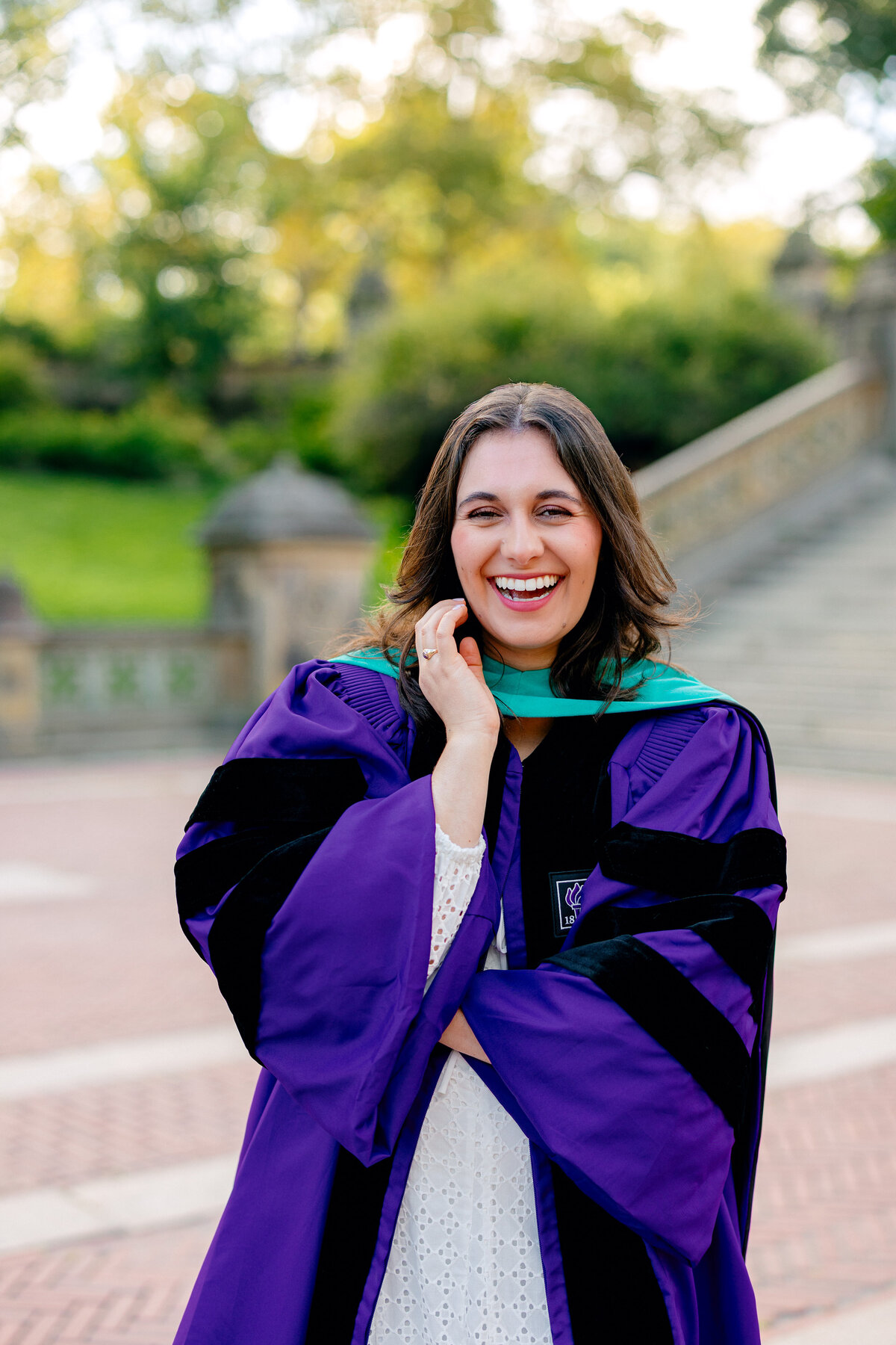 NYU graduate laughing at the camera in purple gown during sunrise at Central Park.