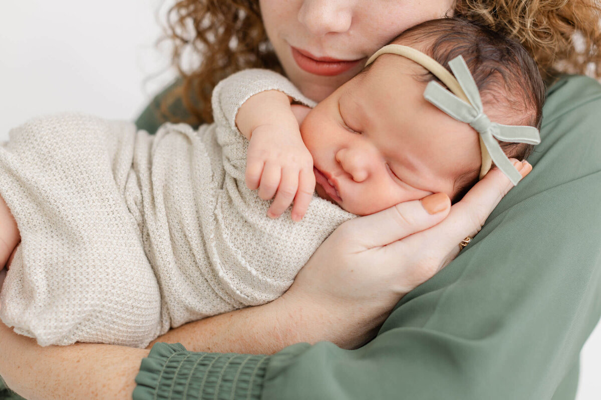 close up of baby's face while mom is holding her in her arms. Mom is wearing a green dress and baby has a green velvet bow on her head.