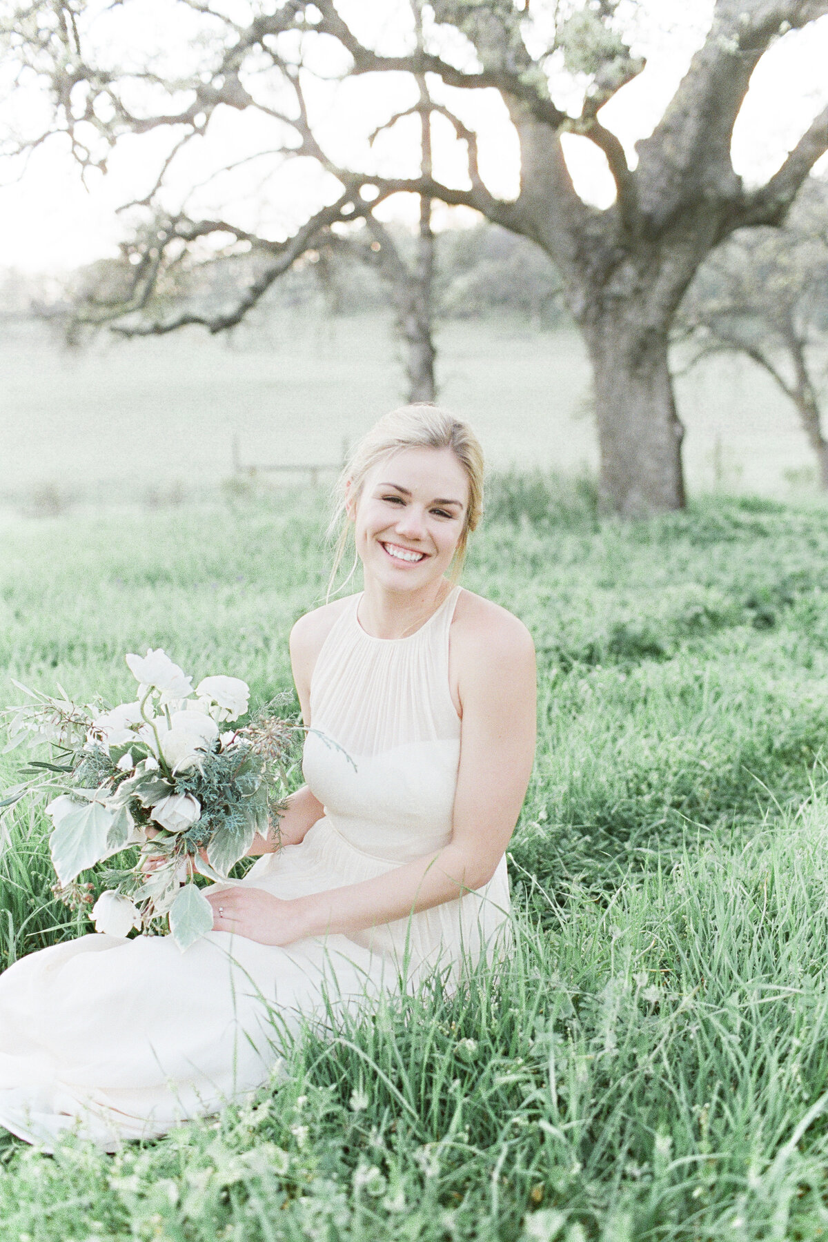 Bride holding flowers while sitting in grass and looking up