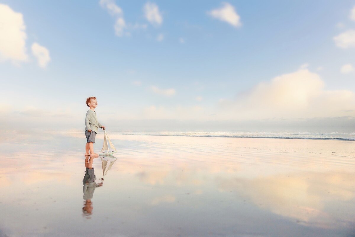 photo of a young boy on the beach with glassy wet sand and a soft pastel sunset