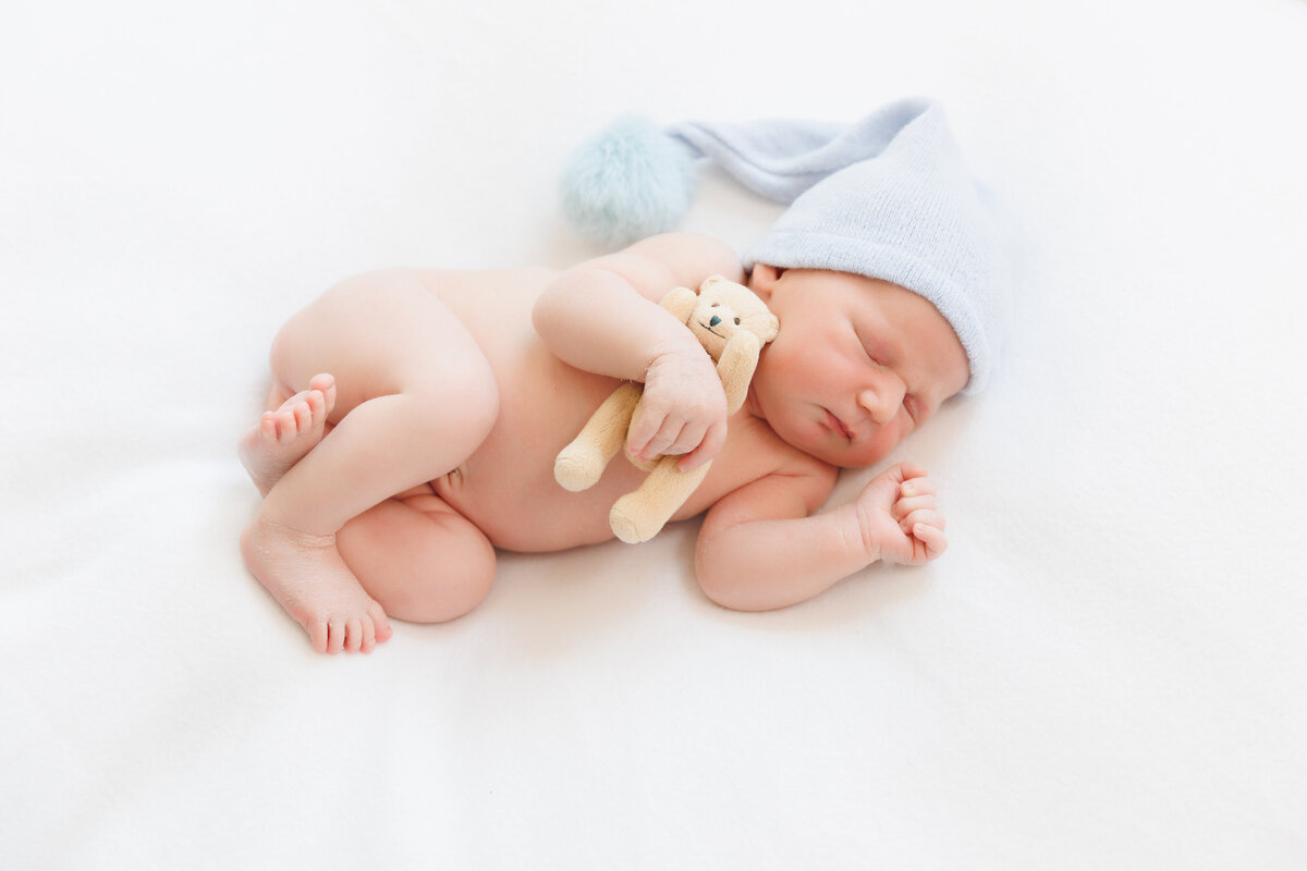 Newborn wearing a blue bonnet holding a teddy bear