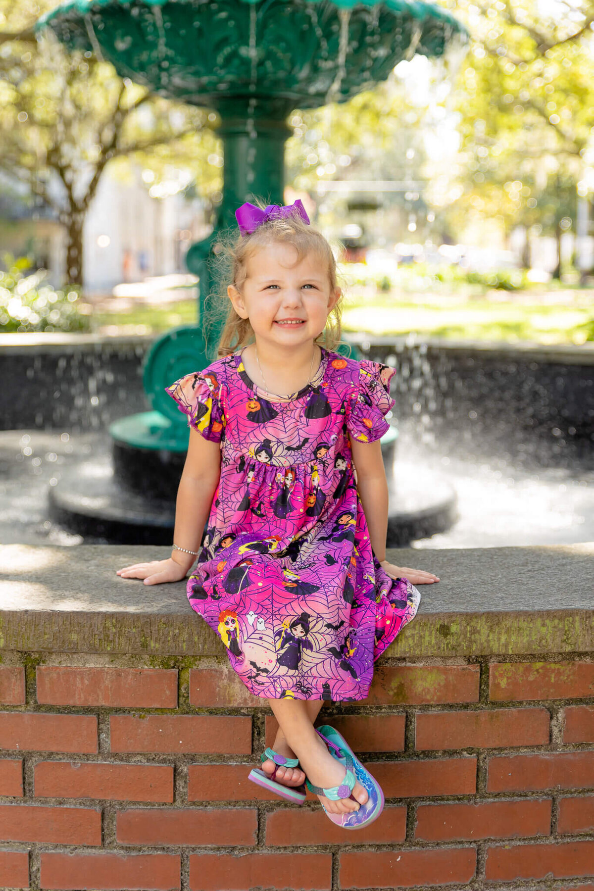 little girl wearing a purple and pink dress sitting on the fountain in Lafyette square downtown Savannah, ga
