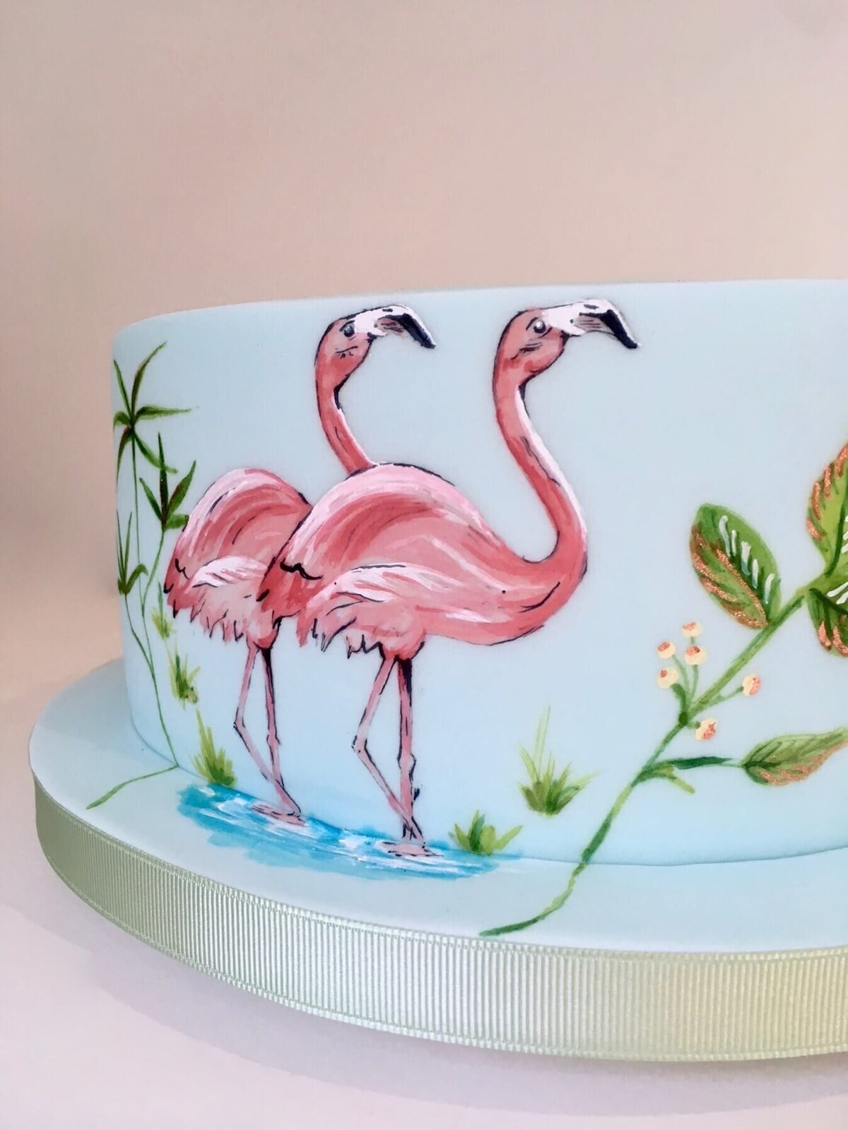 A  close up of a beautiful hand painted cake showing two flamingoes and foliage