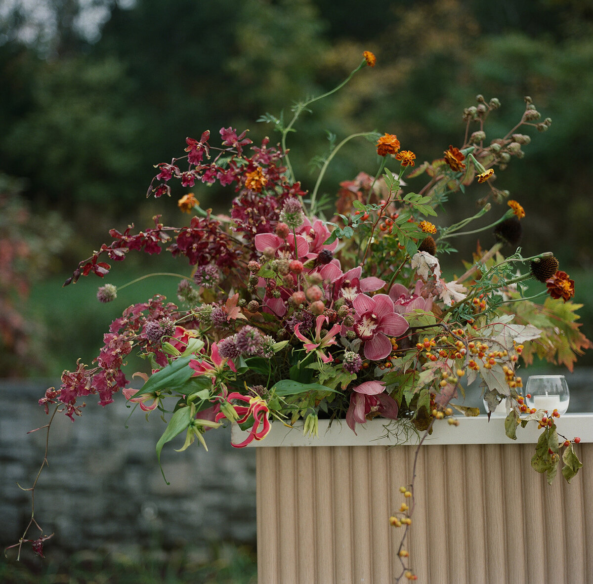 Sculptural ikebana and meadow arrangements decorate the cocktail hour for private estate wedding in Tennessee hills.Clear top tent build out for fall wedding reception in Tennessee hills.  Trailing bar arrangements and floral meadow centerpieces for autumnal wedding reception. Orchids, bittersweet berries, butterfly ranunculus, and tulips are highlighted. Artistic fall color palette in copper, gold, ruby, lavender, and rust. Design by Rosemary & Finch Floral Design in Nashville, TN.