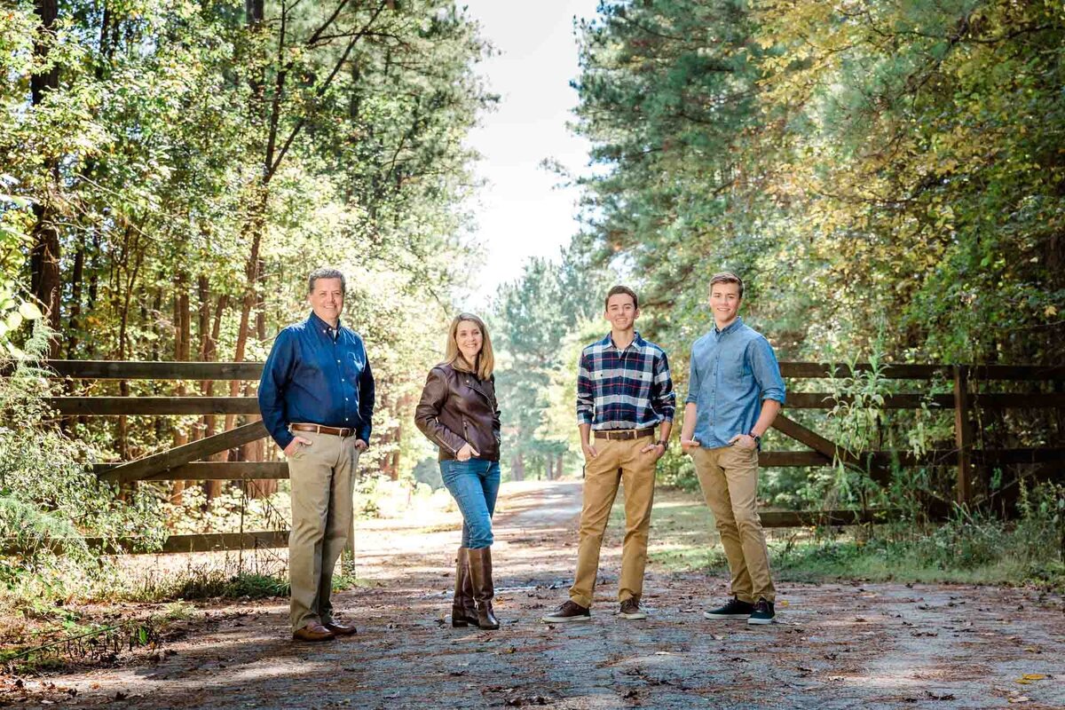 A family portrait with four people standing with attitude in front of a fence.