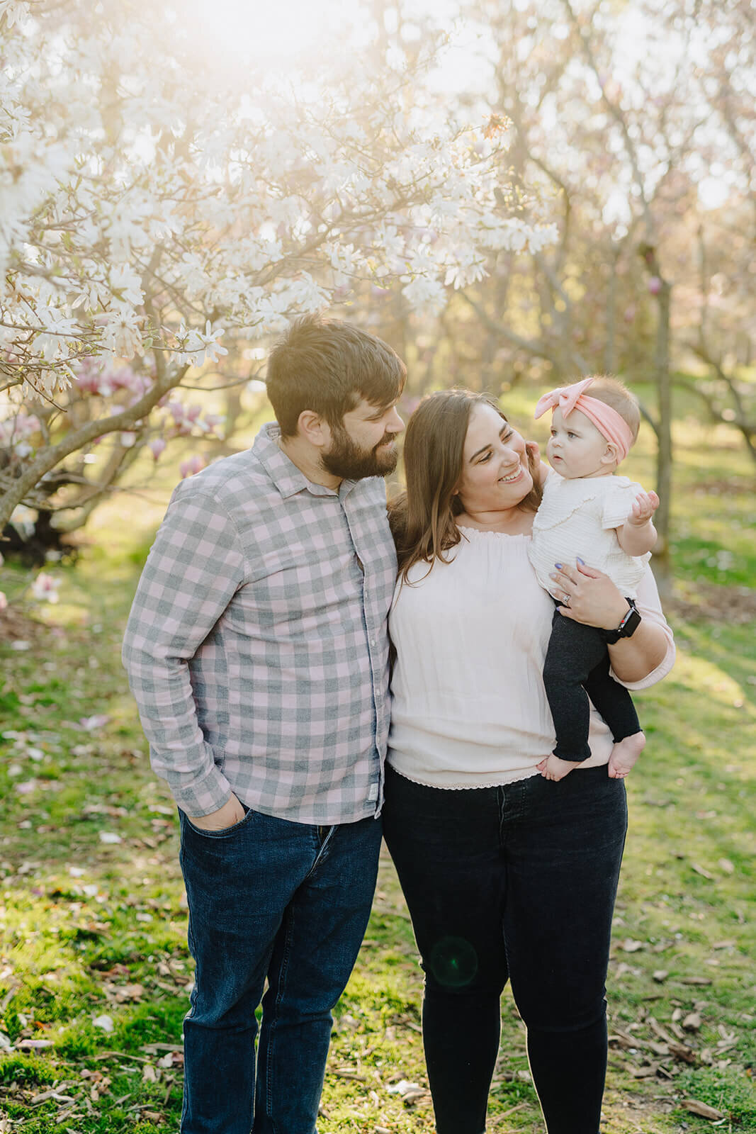 couple holding a baby standing in front of cherry blossom tree