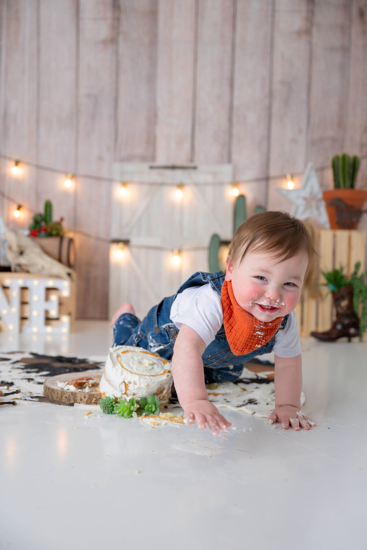 Toddler smashing cake with his knee as he crawls away from his cowboy theme backdrop.