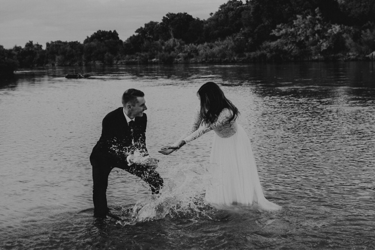 bride and groom in wedding attire playing in river