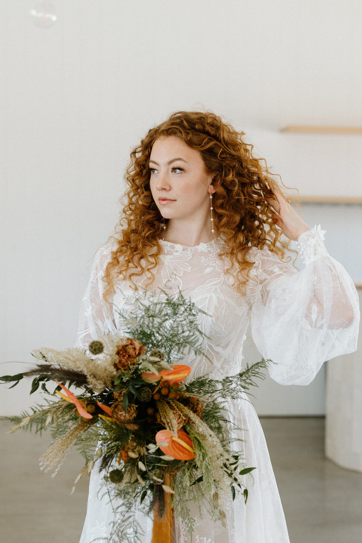 A bride fixes her curly hair while holding her leaf bouquet