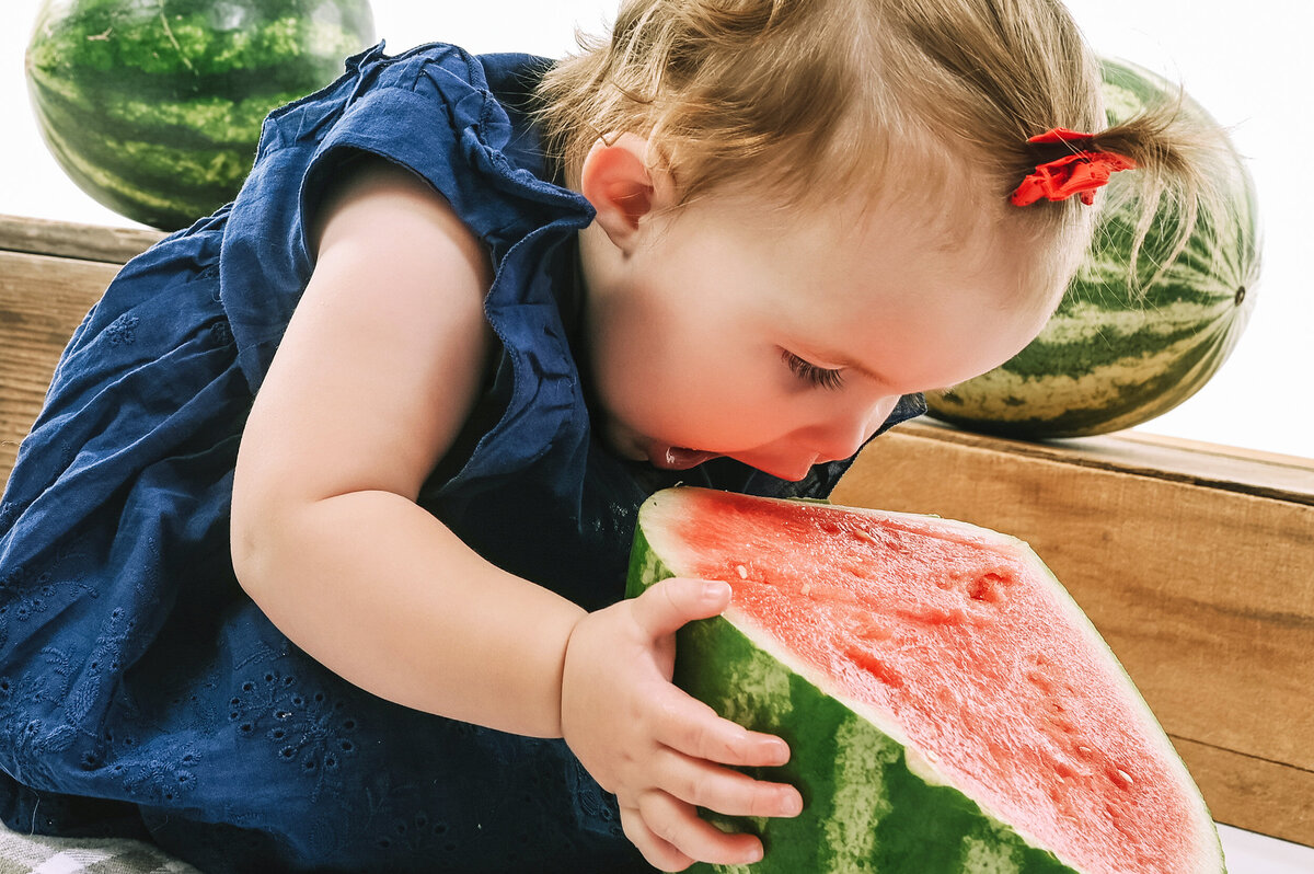 Little girl gets ready to take a big bite as she’s surrounded by watermelon