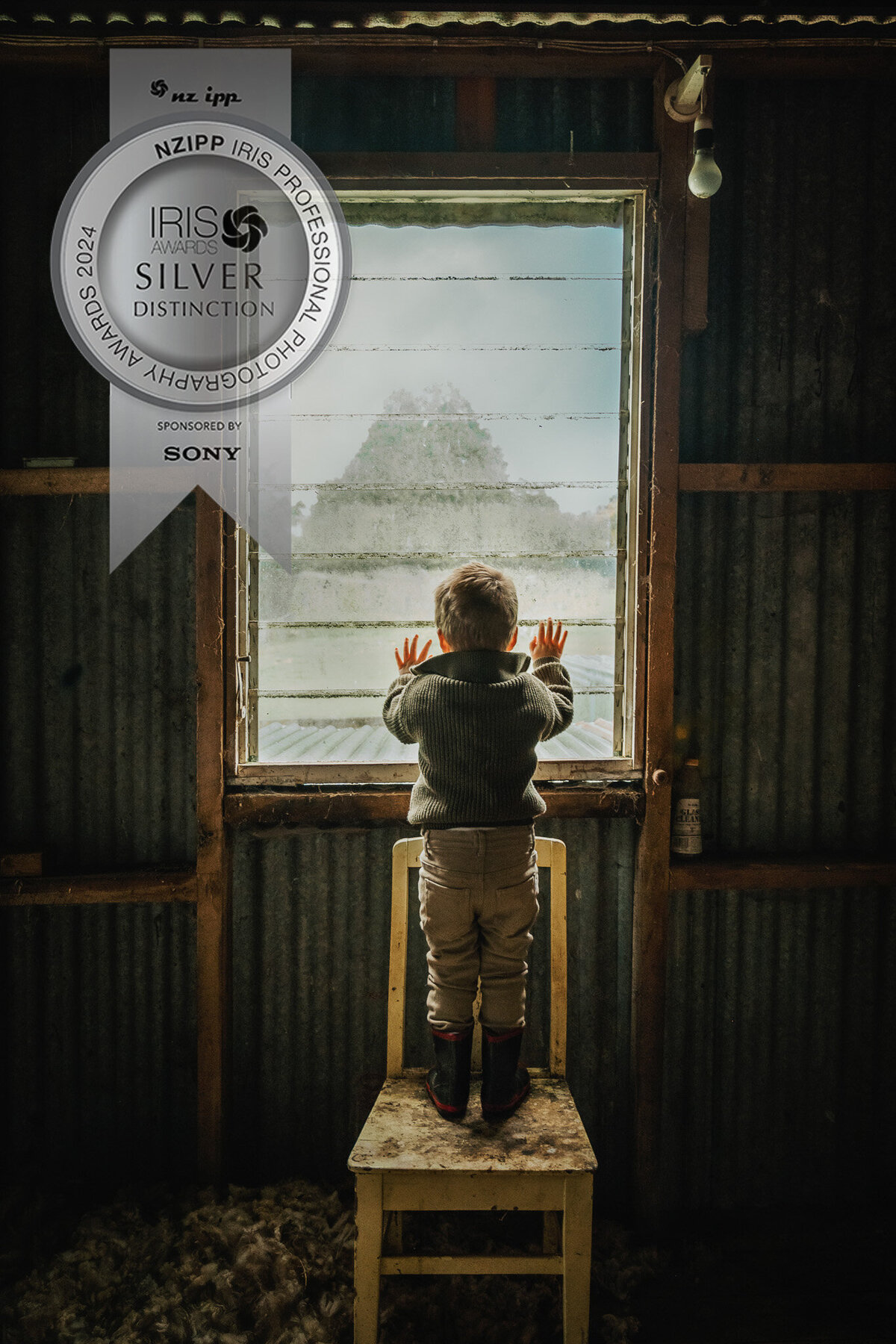 little boy standing on a yellow chair looking out a window at a mountain