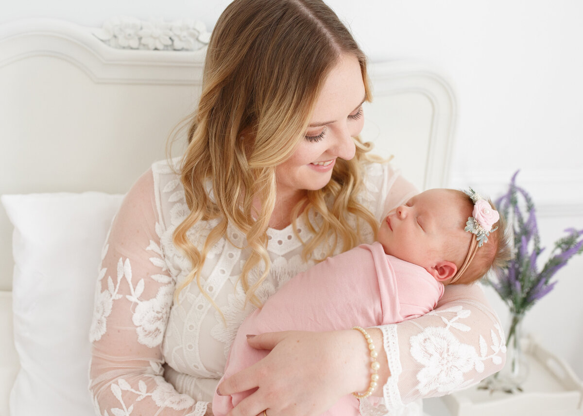 mom in white lace dress cuddling her baby girl on a bed in yorktown photography studio