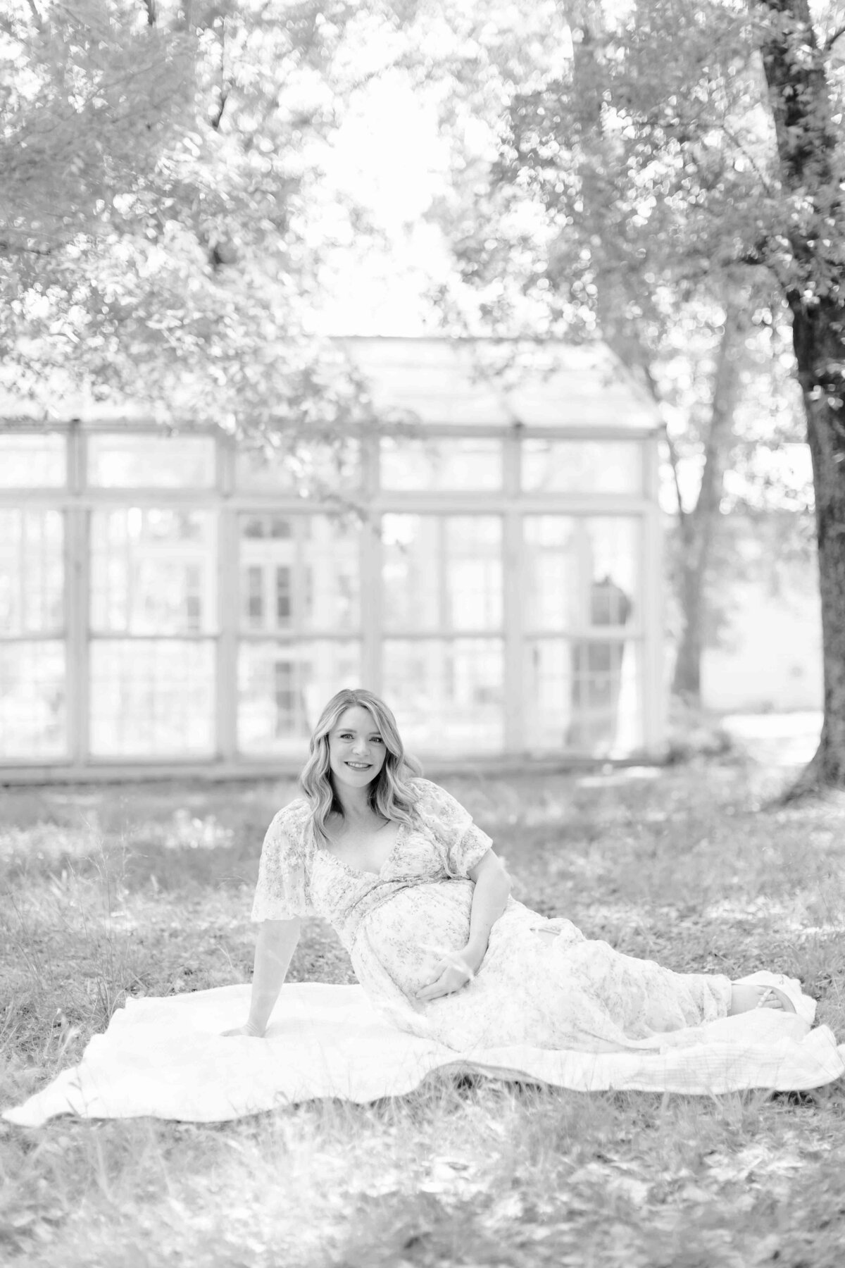 mom lays on white blanket holding her belly for maternity session