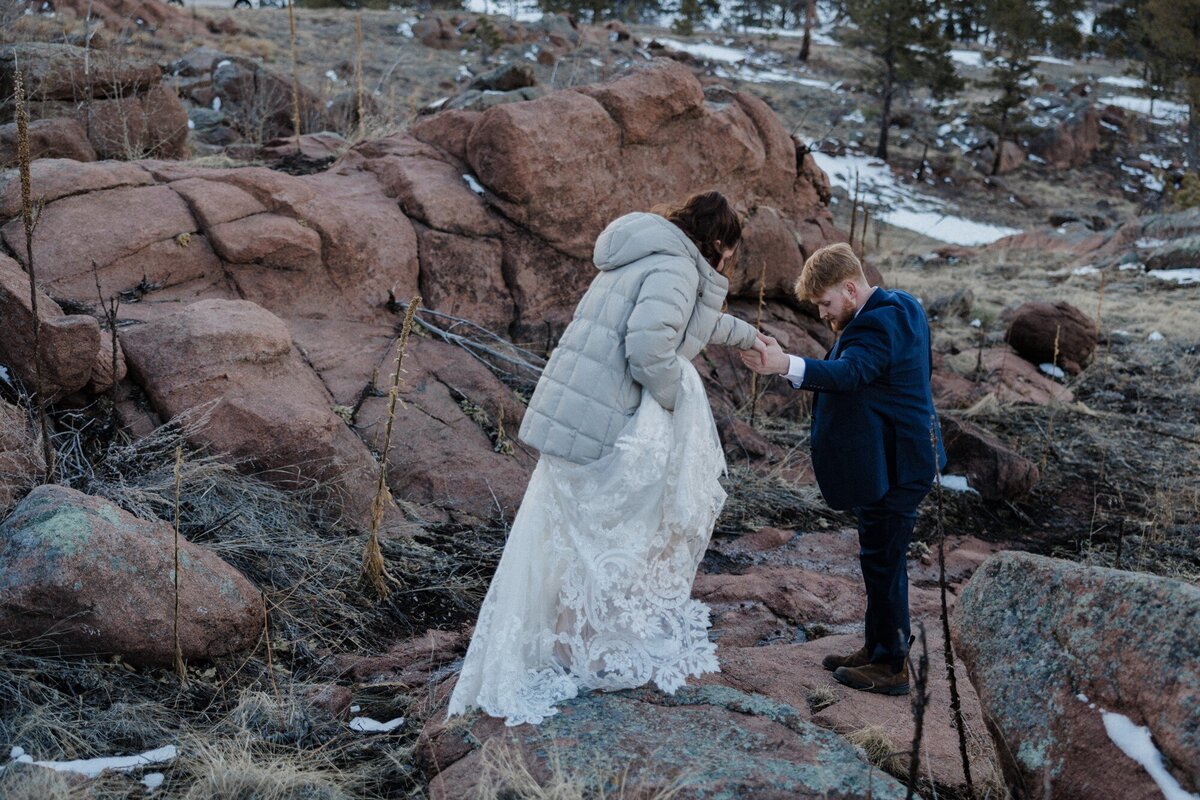 Groom helps bride during hiking elopement.