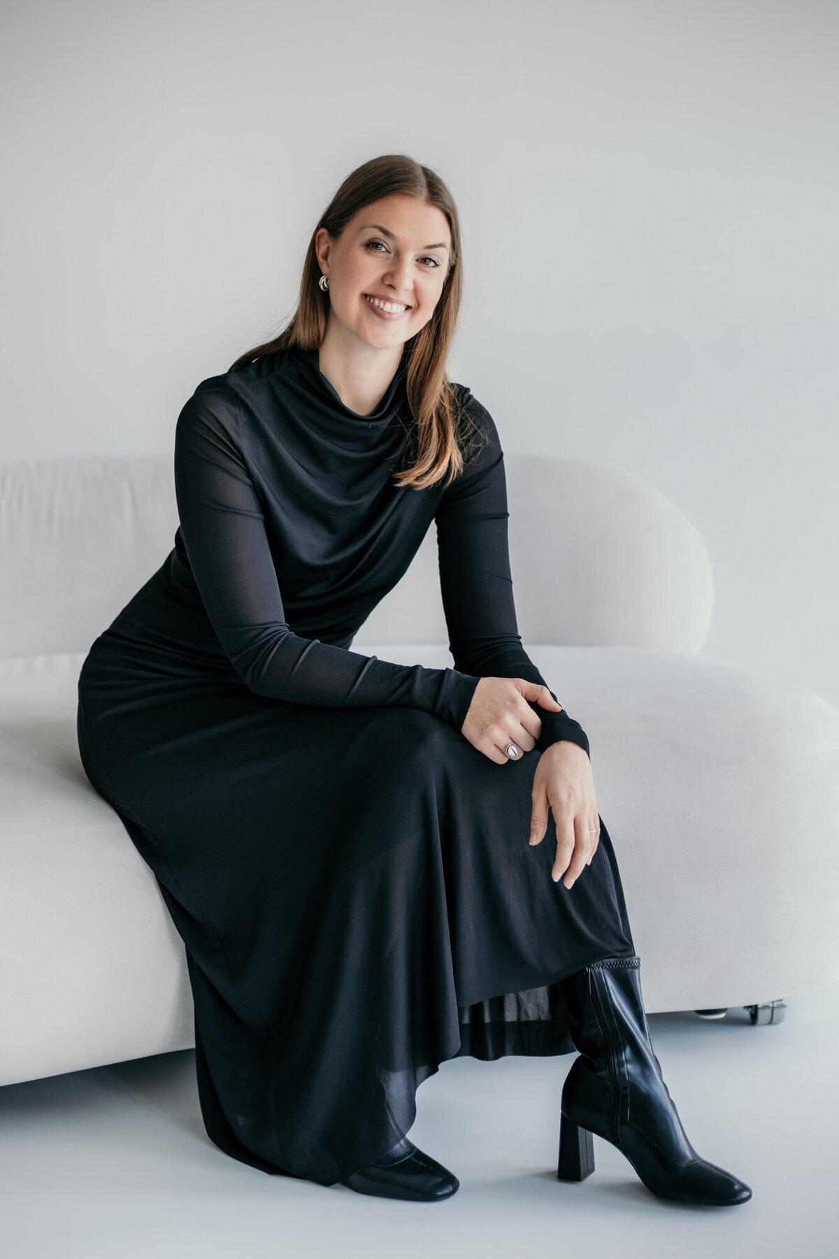 Smiling woman in a long black dress sits on a sofa.