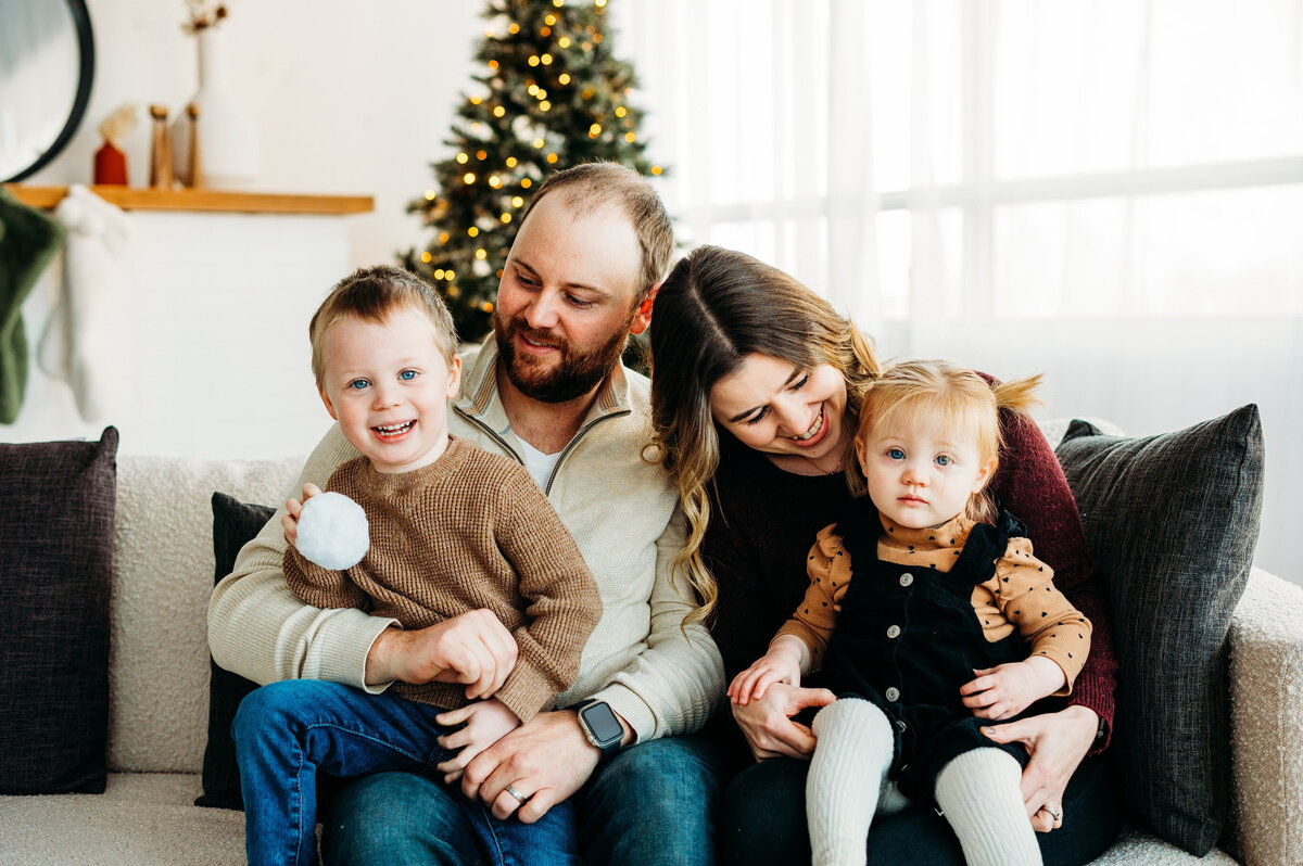 Parents and children smiling together by Christmas tree during Ottawa holiday studio mini session.