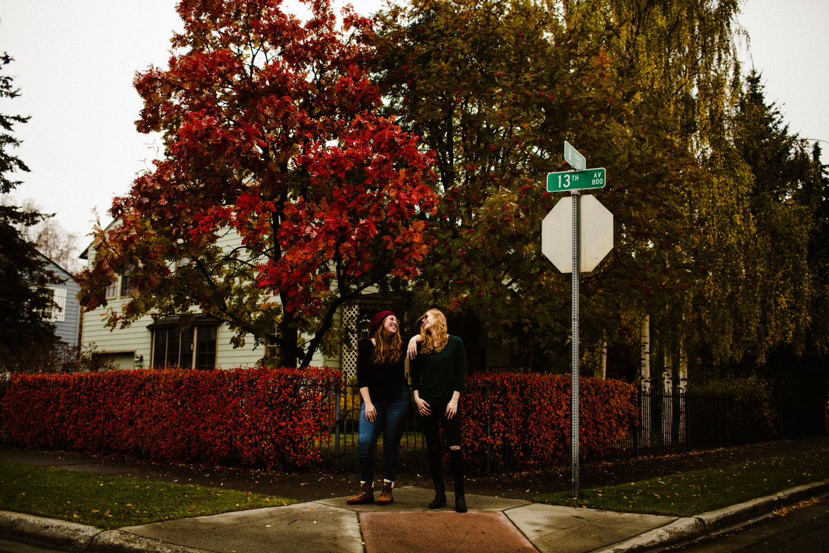 sisters stand on corner looking at one another surrounded by fall leaves
