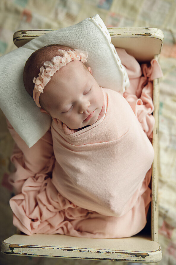 Newborn wrapped in pink sleeps in a little bed at the studio at Angela Marie Media.