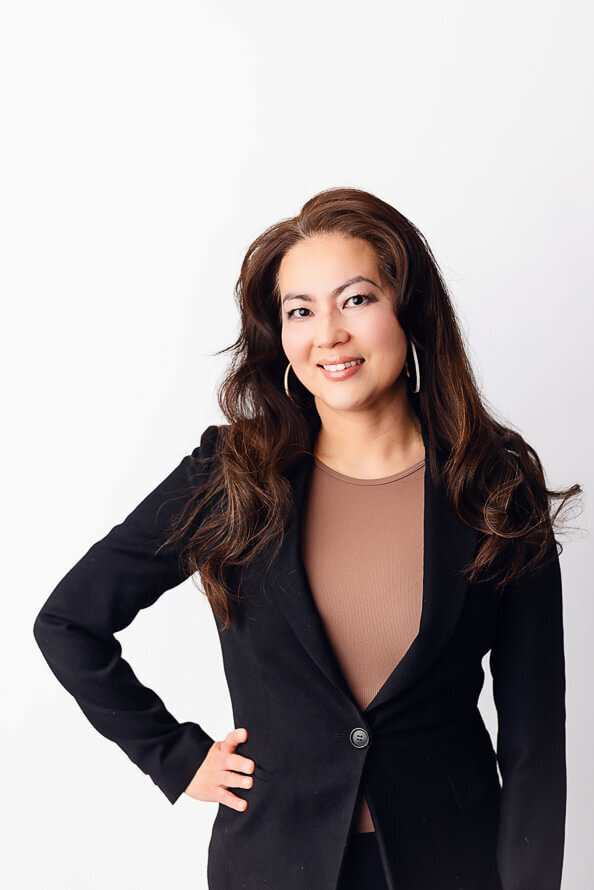 Moan in black jacket poses with hand on hip in white studio.