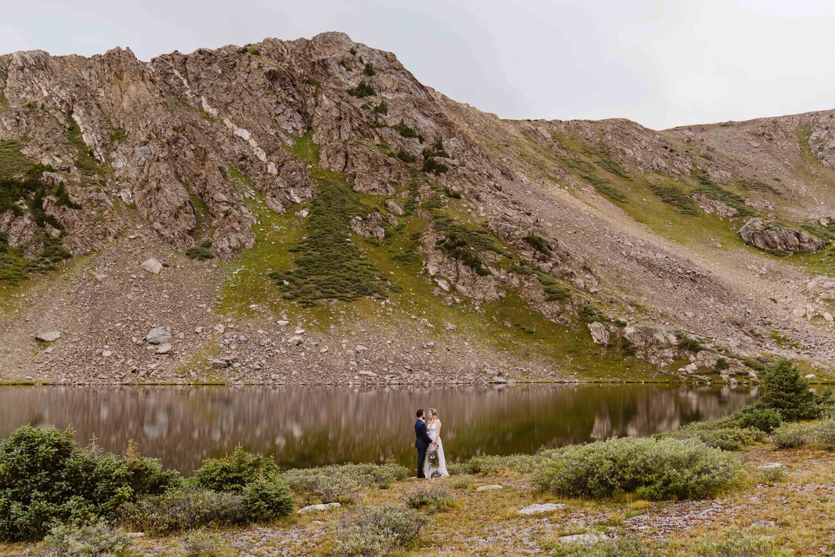 Couple stands at the foot of an alpine lake during their Aspen, Colorado elopement.