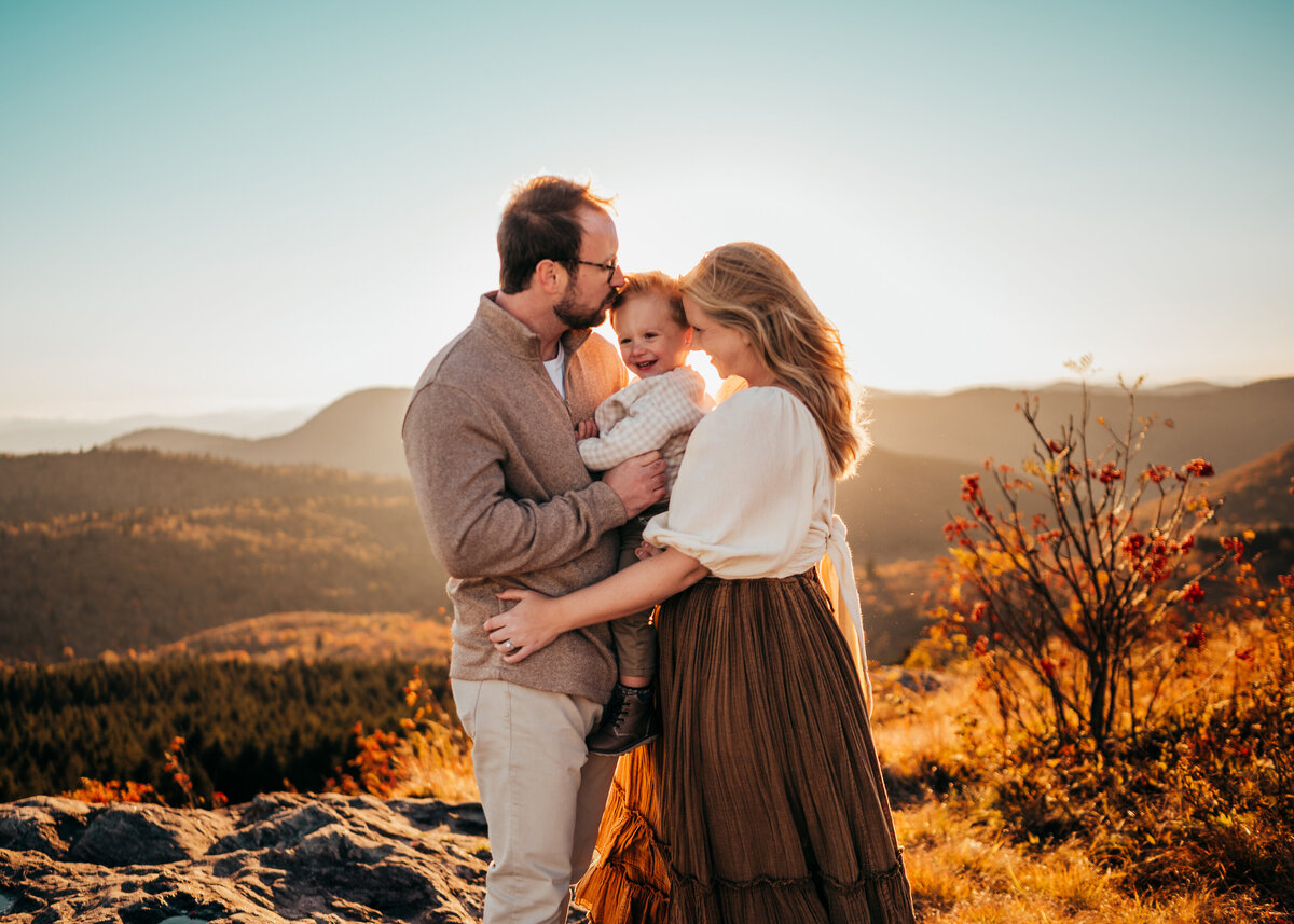 family of three cuddle on top of mountain at sunset in North Carolina